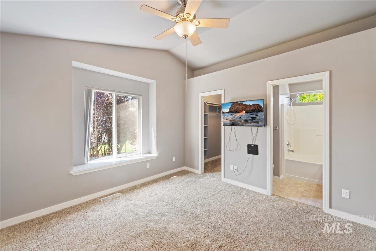 Unfurnished bedroom featuring a walk in closet, carpet flooring, lofted ceiling, connected bathroom, and a ceiling fan