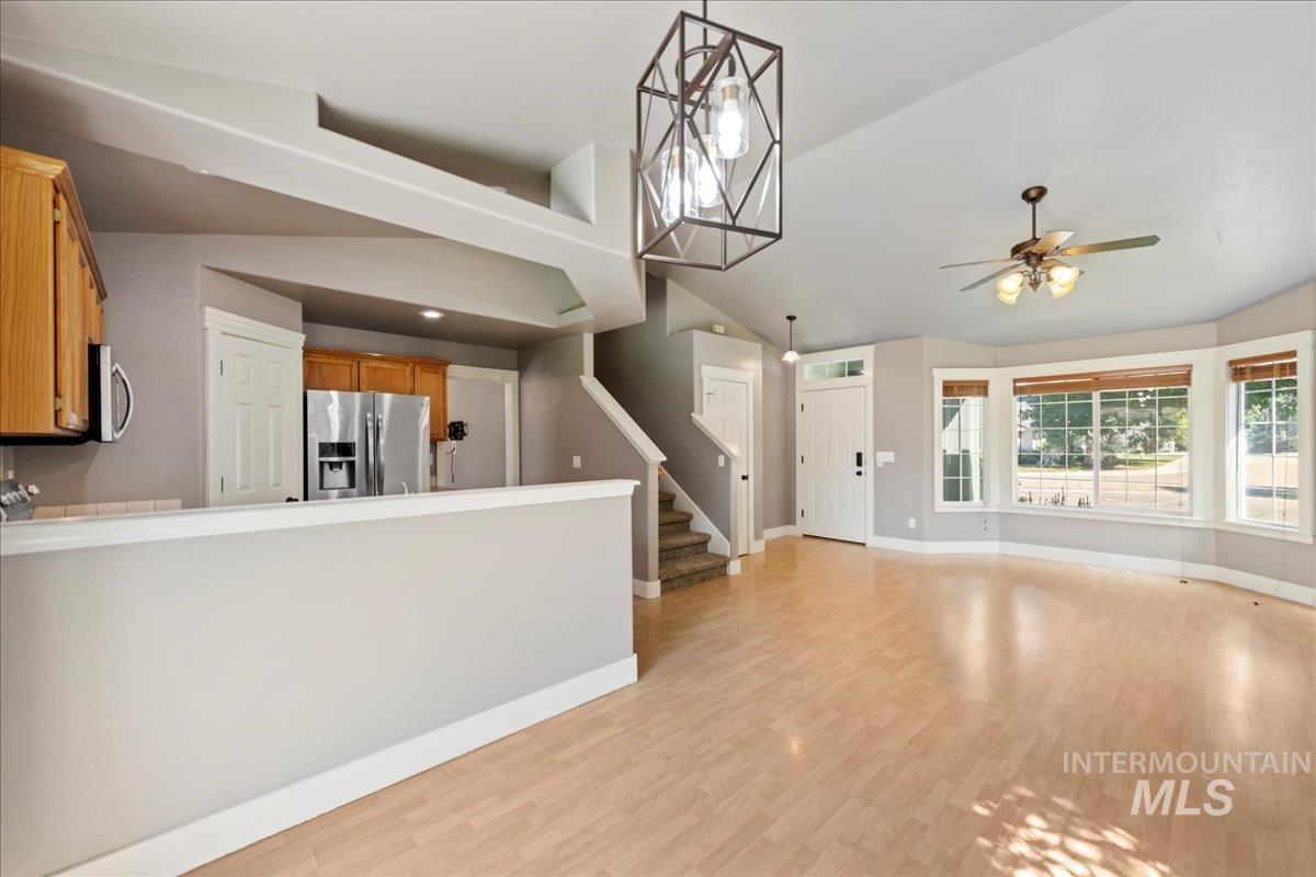 Unfurnished living room featuring light wood-type flooring, ceiling fan, stairway, and lofted ceiling