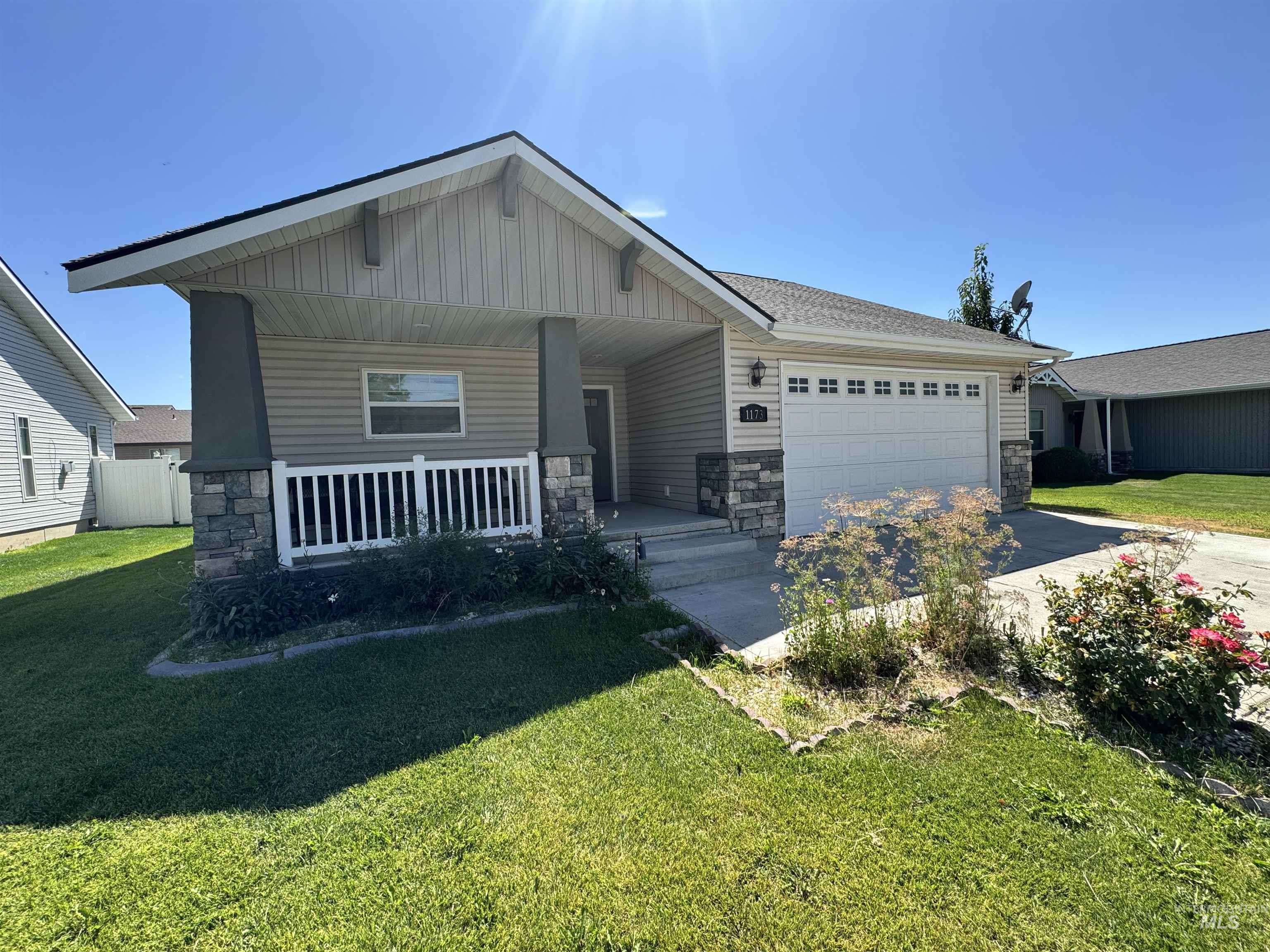 View of front of house featuring stone siding, a porch, an attached garage, concrete driveway, and a front lawn