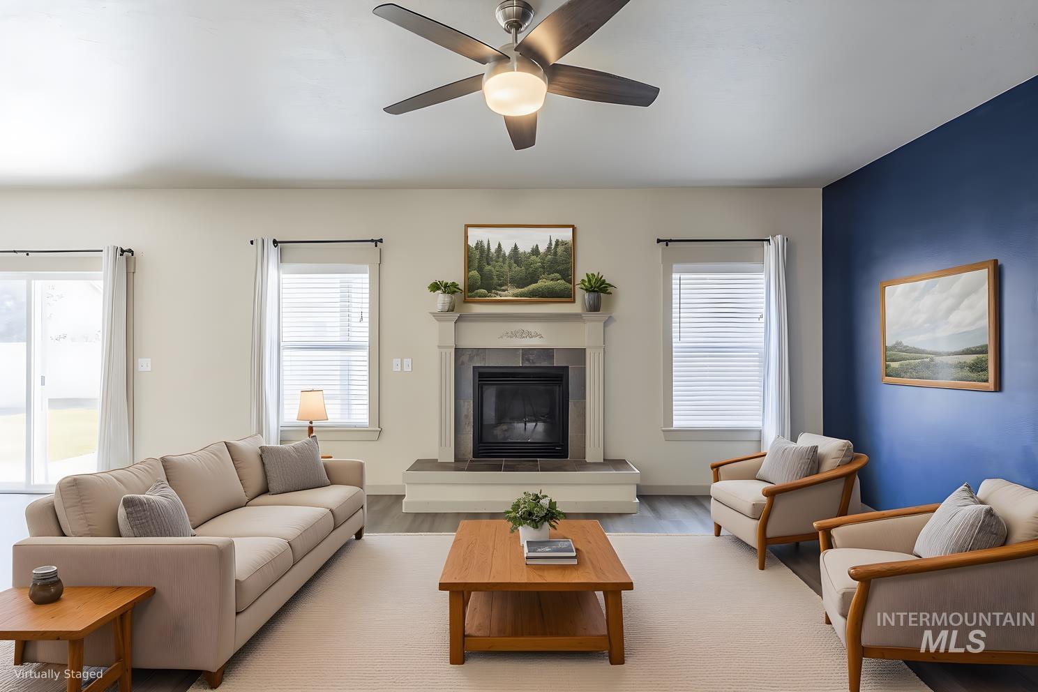 Living room with wood finished floors, a tiled fireplace, and a ceiling fan