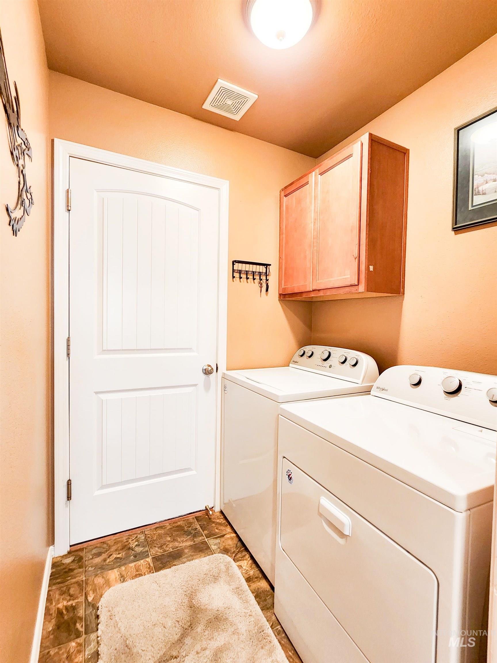 Laundry room with washing machine and clothes dryer, cabinet space, and stone finish floors