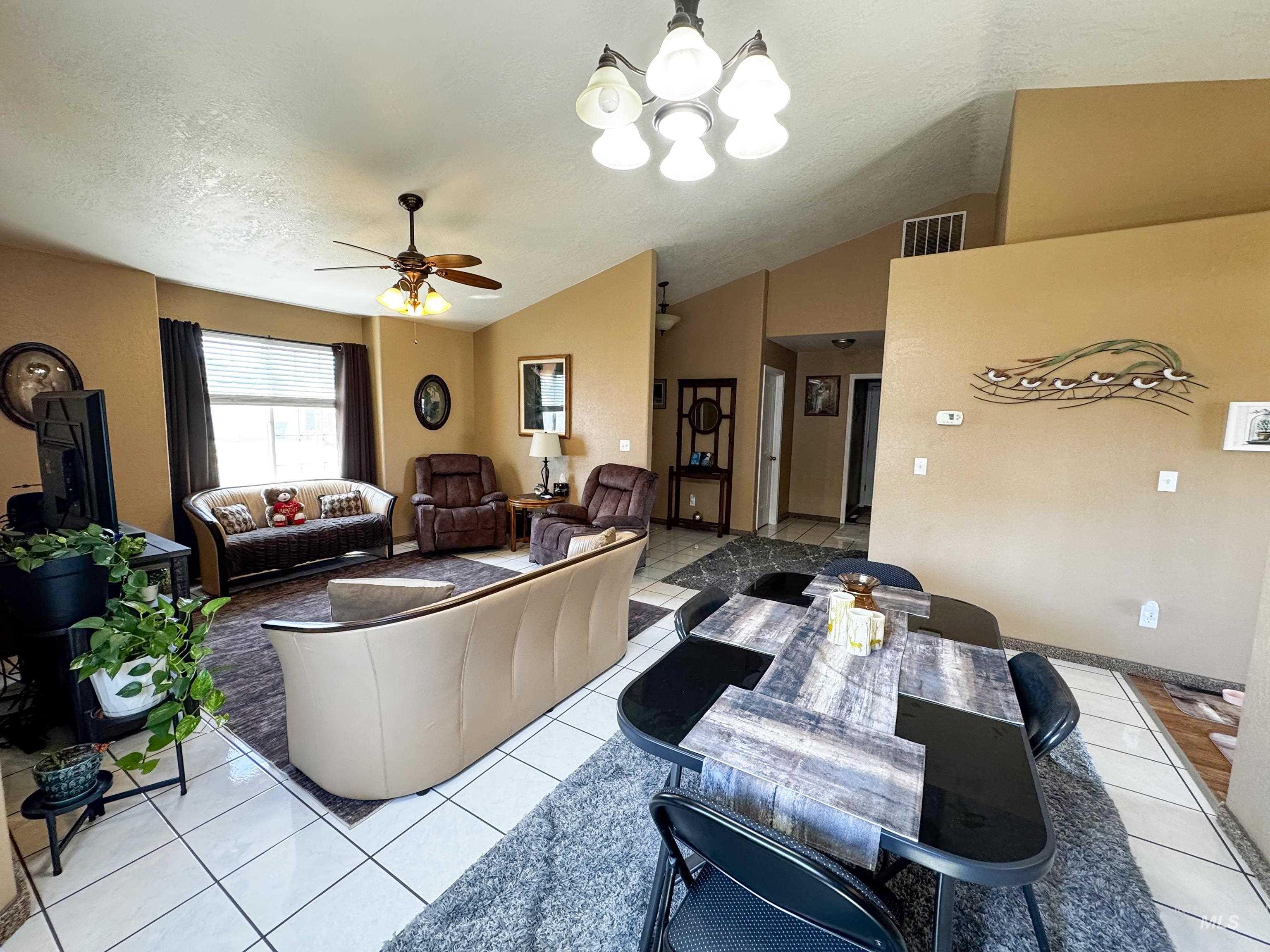 Living room featuring ceiling fan, a textured ceiling, light tile patterned floors, a chandelier, and vaulted ceiling
