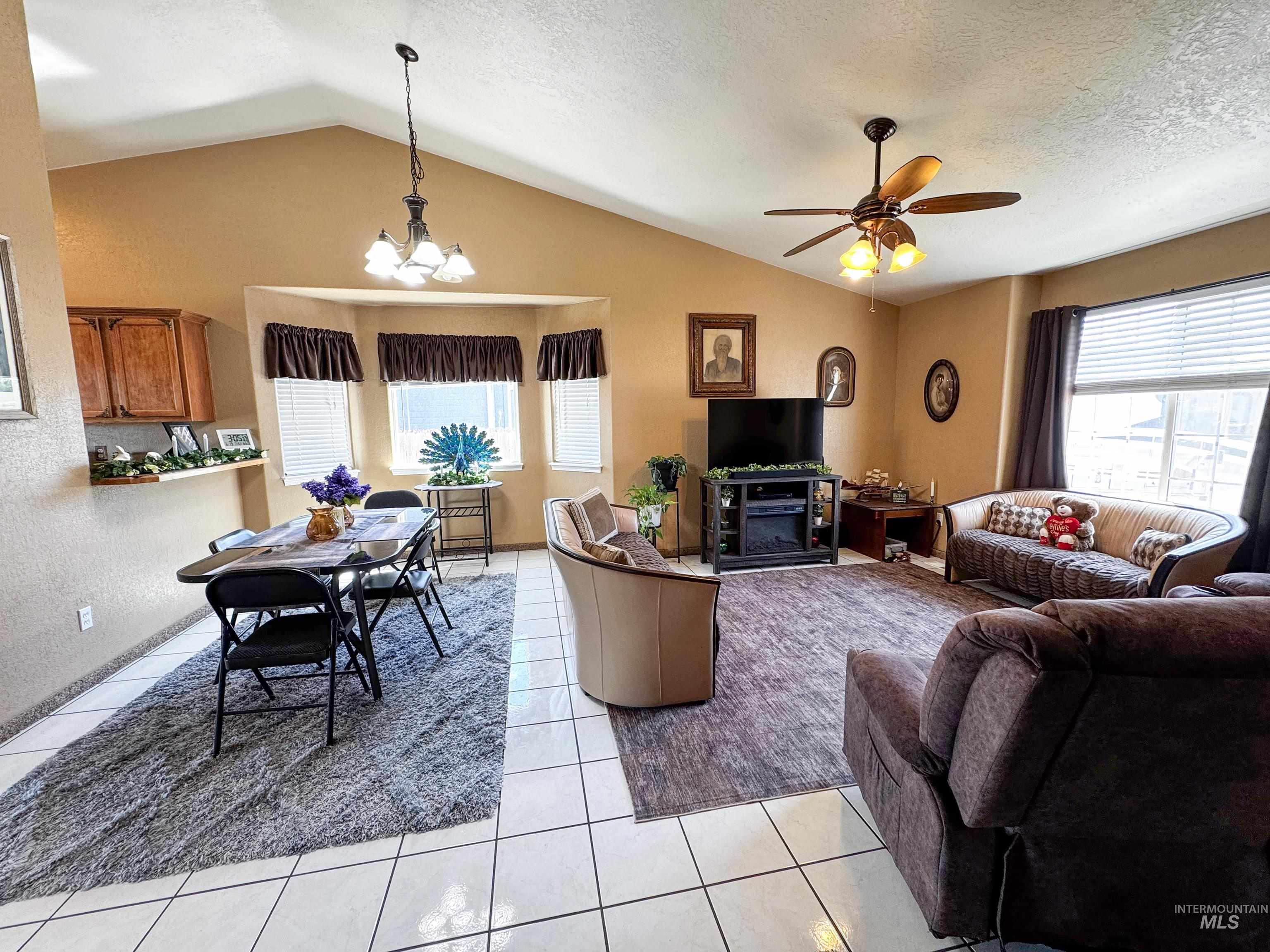Living room with lofted ceiling, a chandelier, light tile patterned flooring, and a ceiling fan