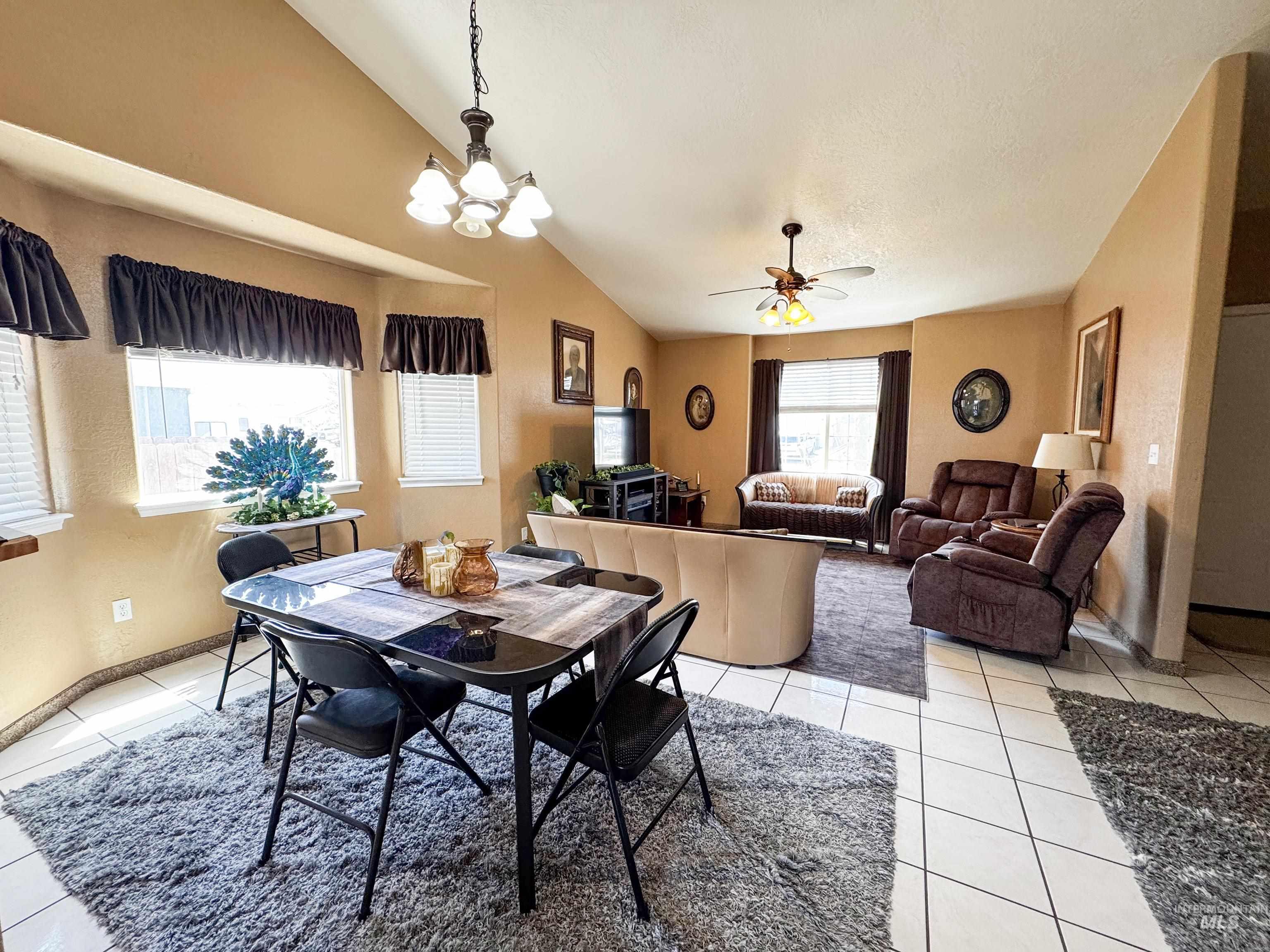 Dining space with lofted ceiling, light tile patterned floors, a chandelier, and a ceiling fan