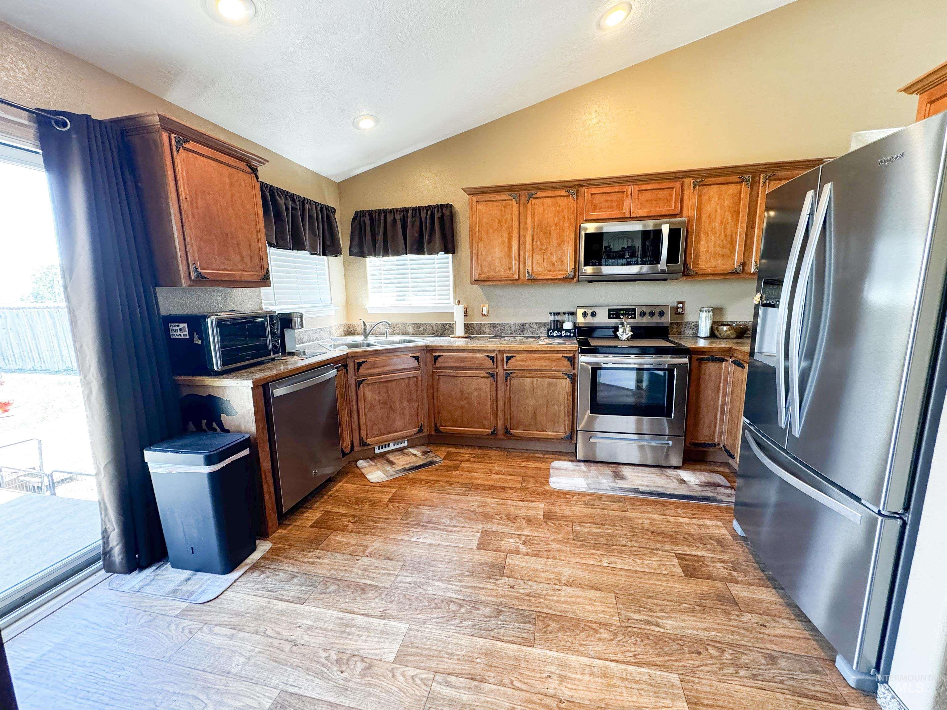 Kitchen featuring stainless steel appliances, vaulted ceiling, brown cabinets, light wood-style flooring, and recessed lighting