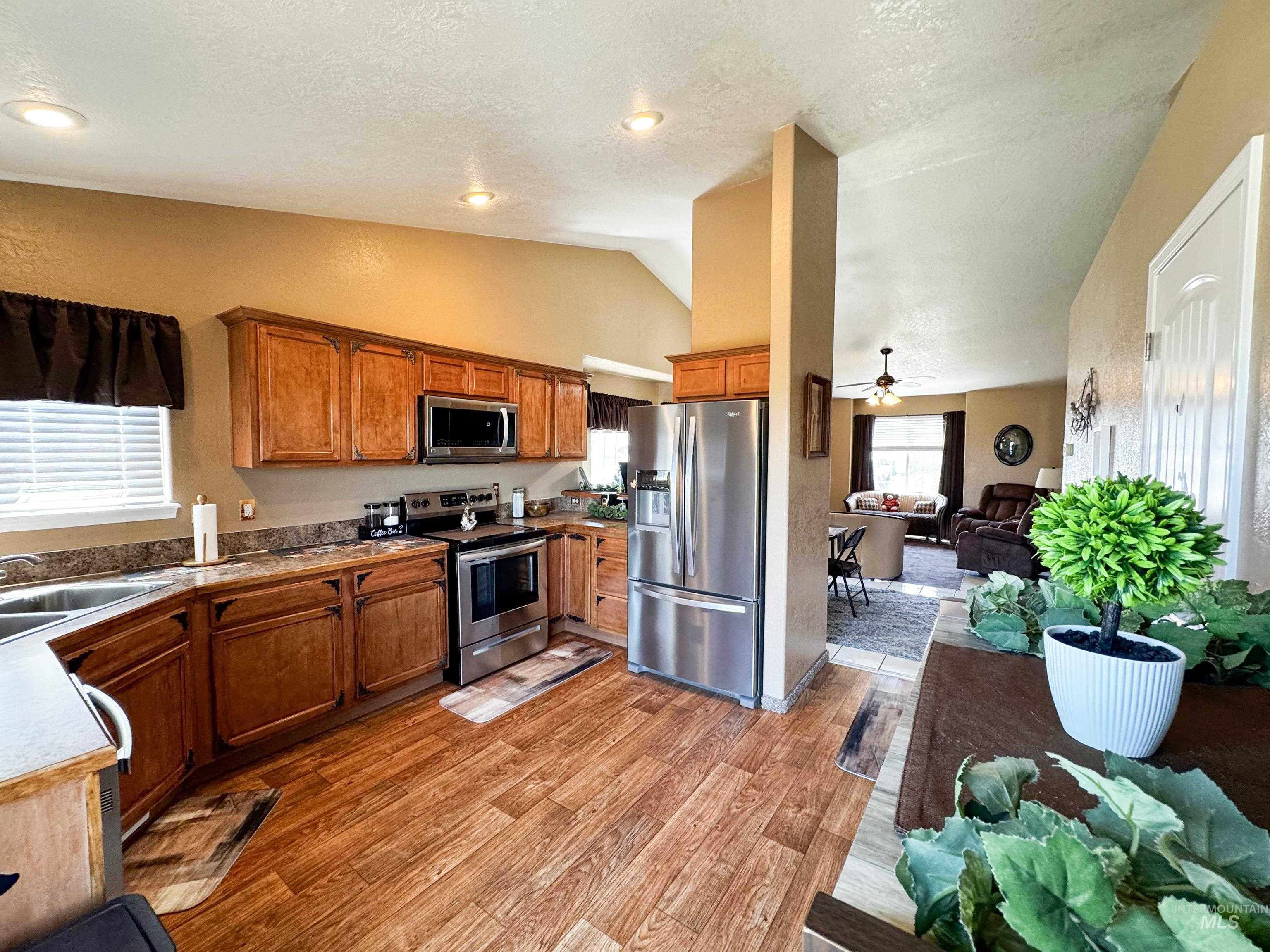 Kitchen with stainless steel appliances, lofted ceiling, a textured ceiling, light wood finished floors, and brown cabinets