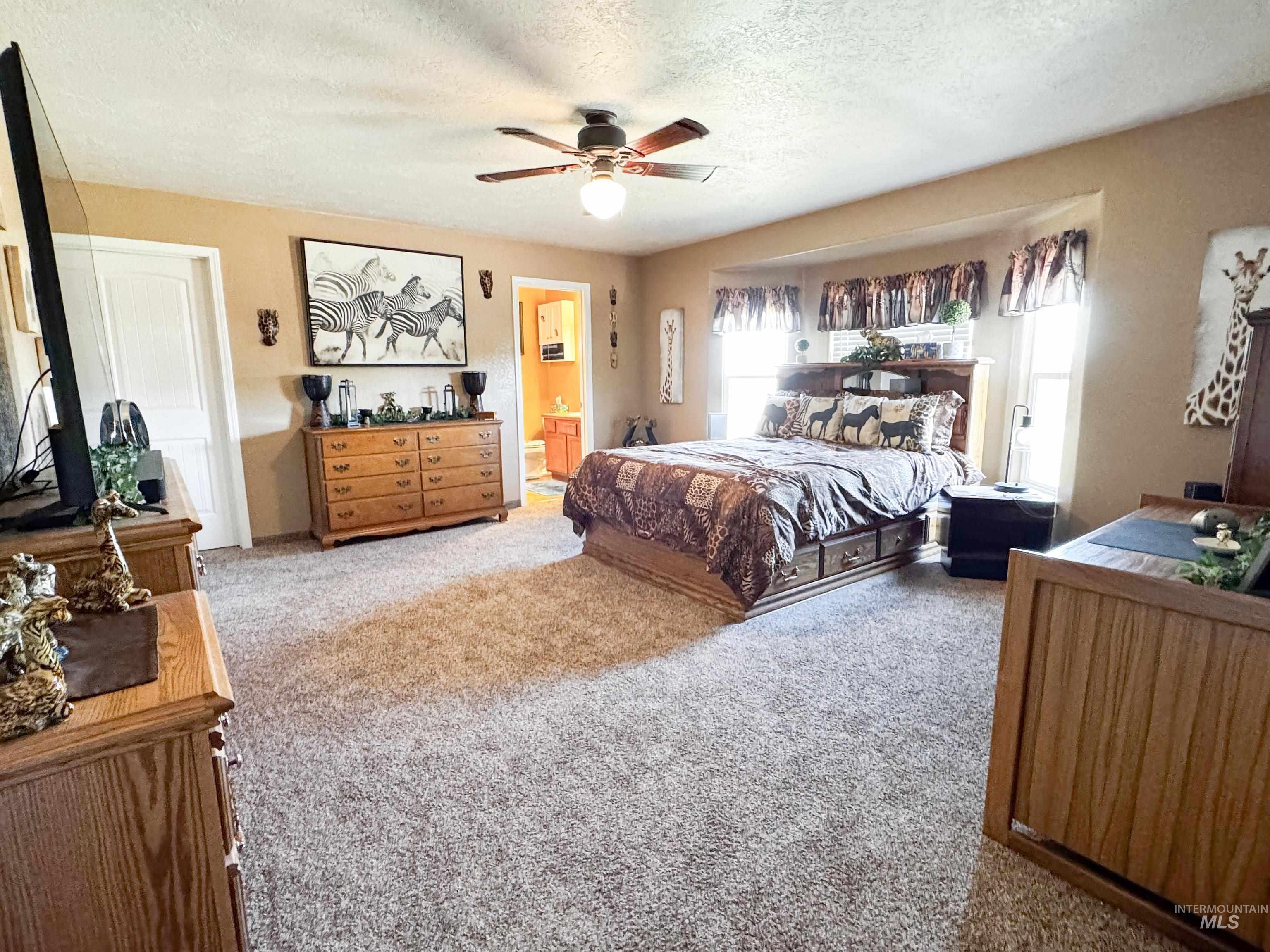 Bedroom with light colored carpet, a textured ceiling, connected bathroom, and ceiling fan