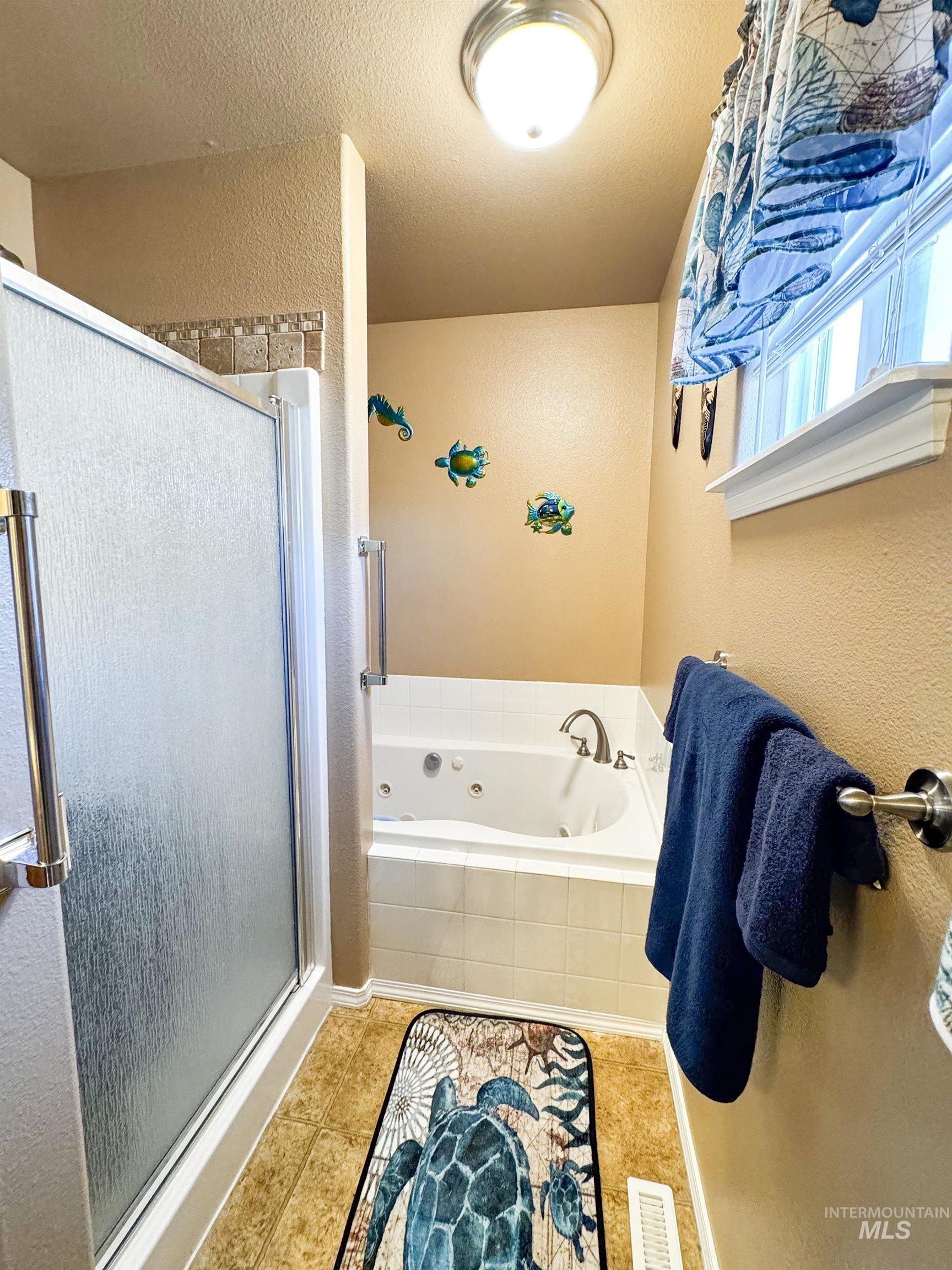 Full bathroom with a stall shower, a whirlpool tub, a textured wall, tile patterned floors, and a textured ceiling