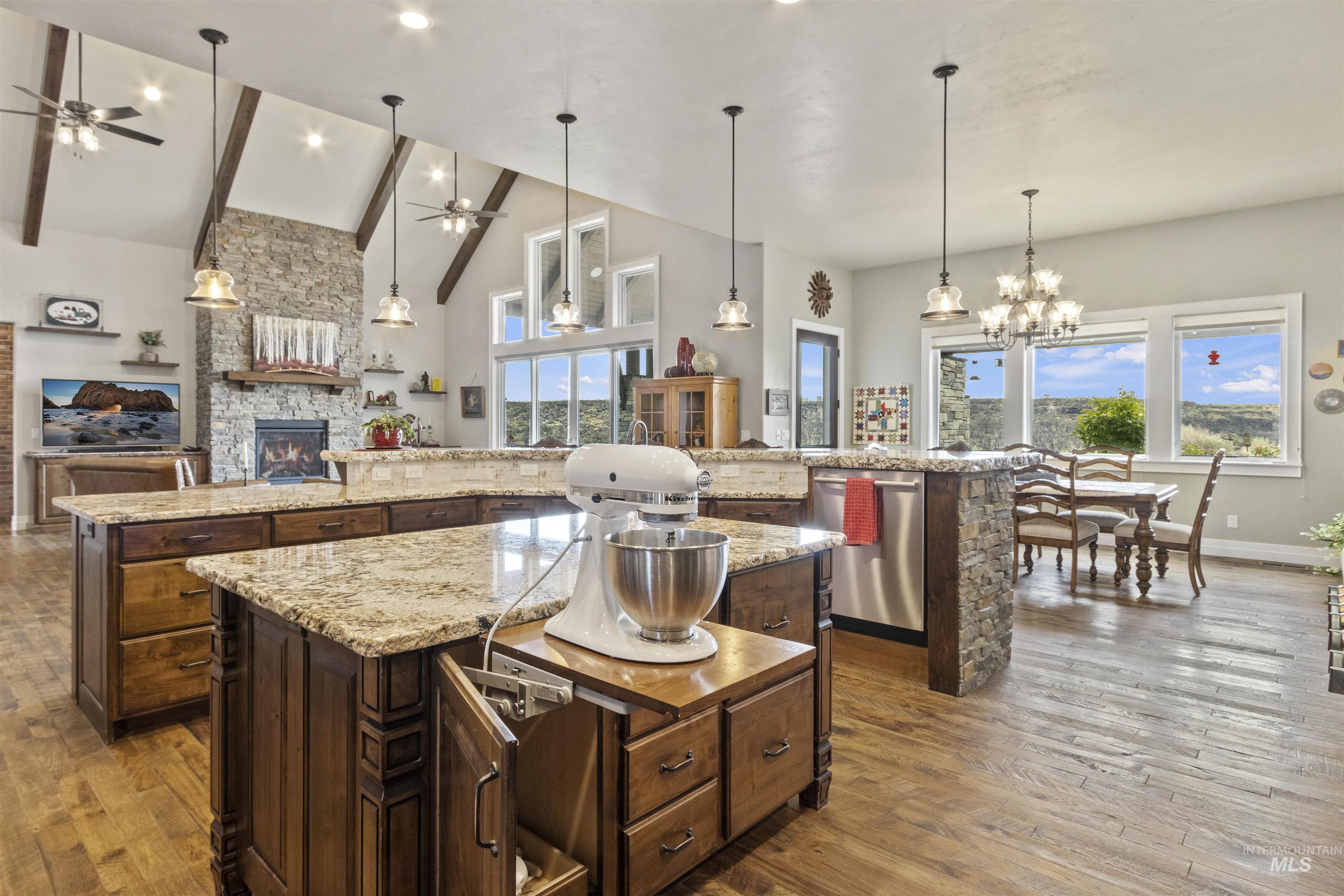 Kitchen with ceiling fan, a large island with sink, a fireplace, wood finished floors, and high vaulted ceiling