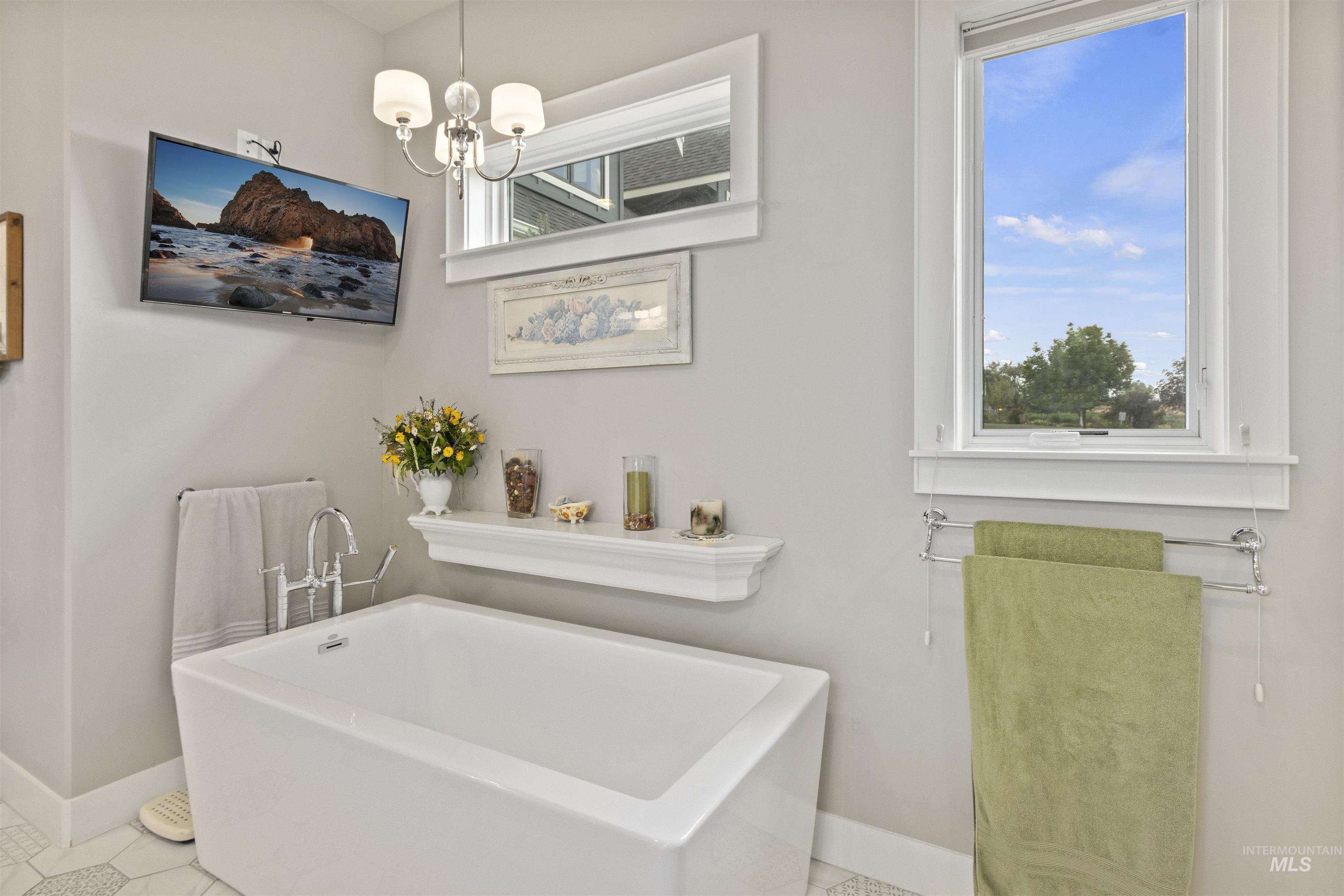 Bathroom featuring a freestanding bath, plenty of natural light, a chandelier, and tile patterned flooring
