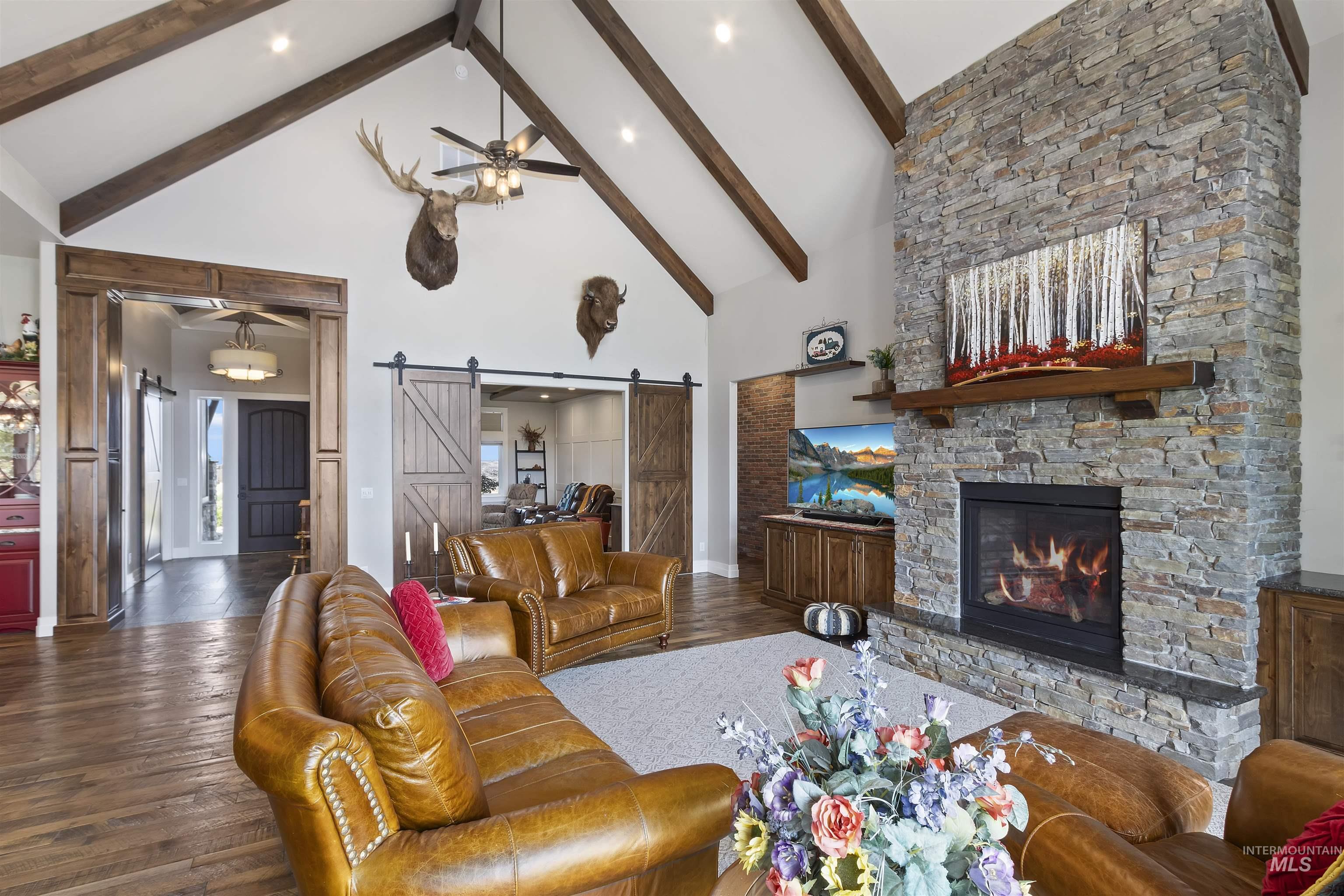 Living room with a barn door, a ceiling fan, high vaulted ceiling, beamed ceiling, and wood finished floors