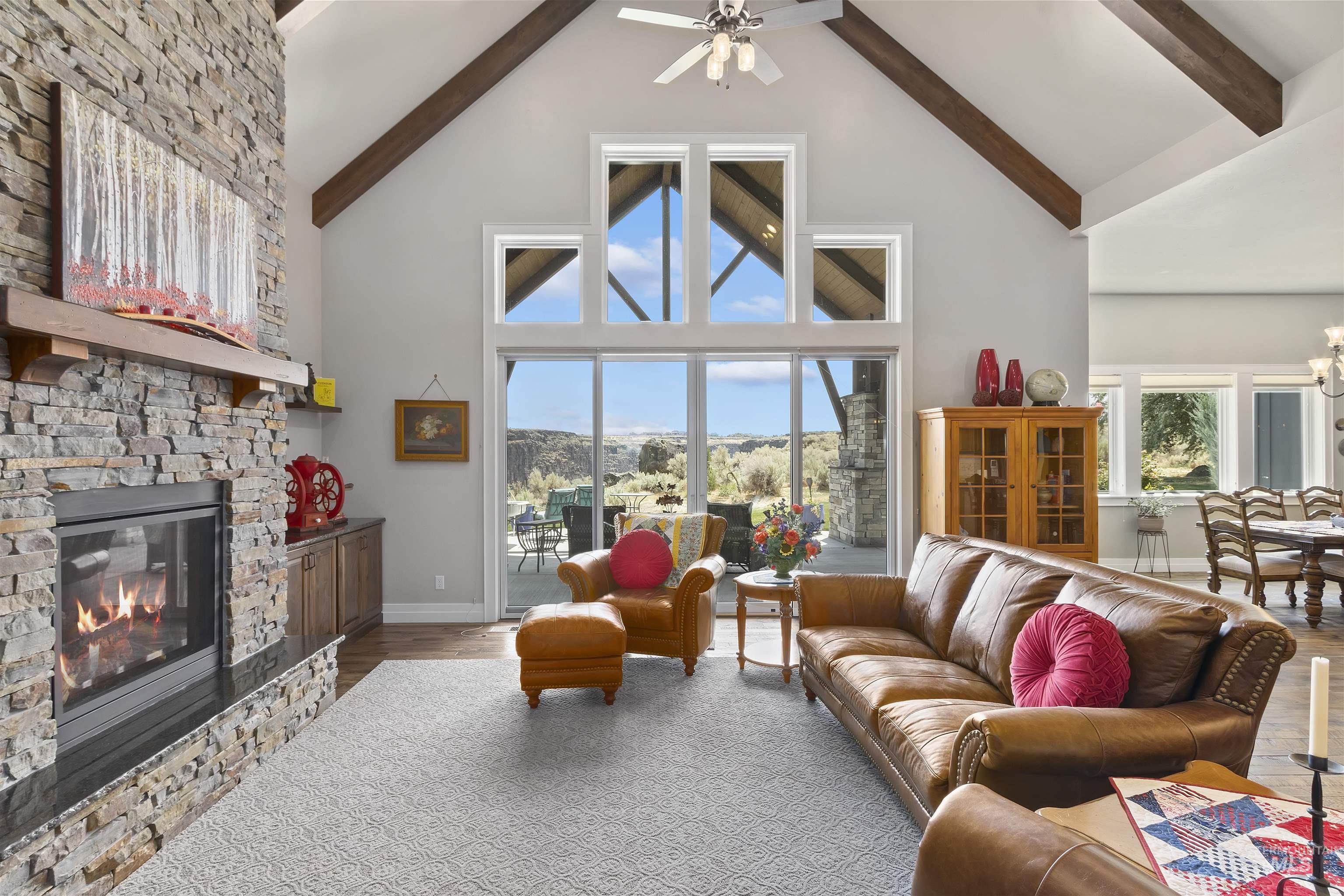 Living area with high vaulted ceiling, beamed ceiling, a ceiling fan, a fireplace, and wood finished floors