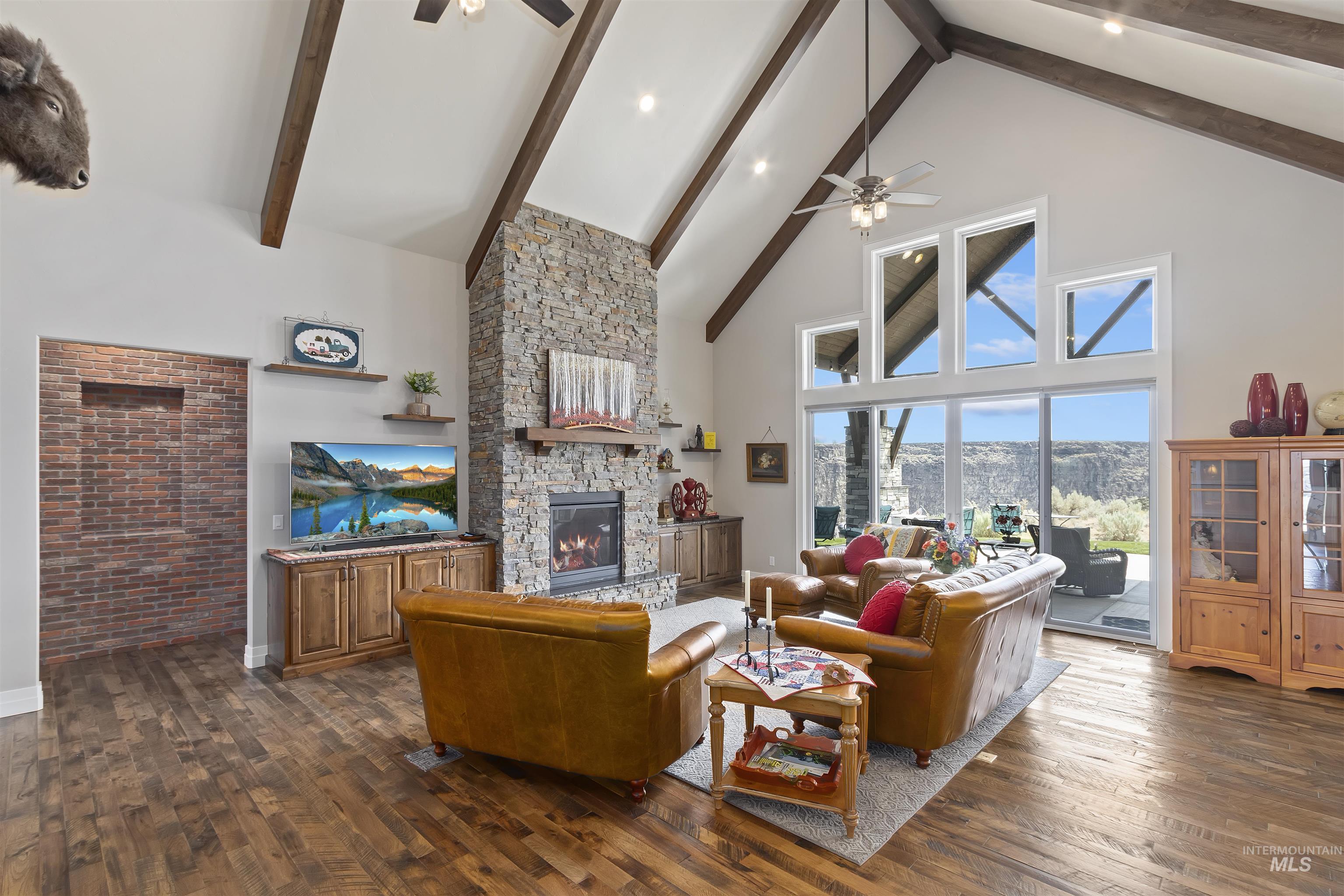 Living area with ceiling fan, high vaulted ceiling, a fireplace, dark wood-style floors, and beamed ceiling