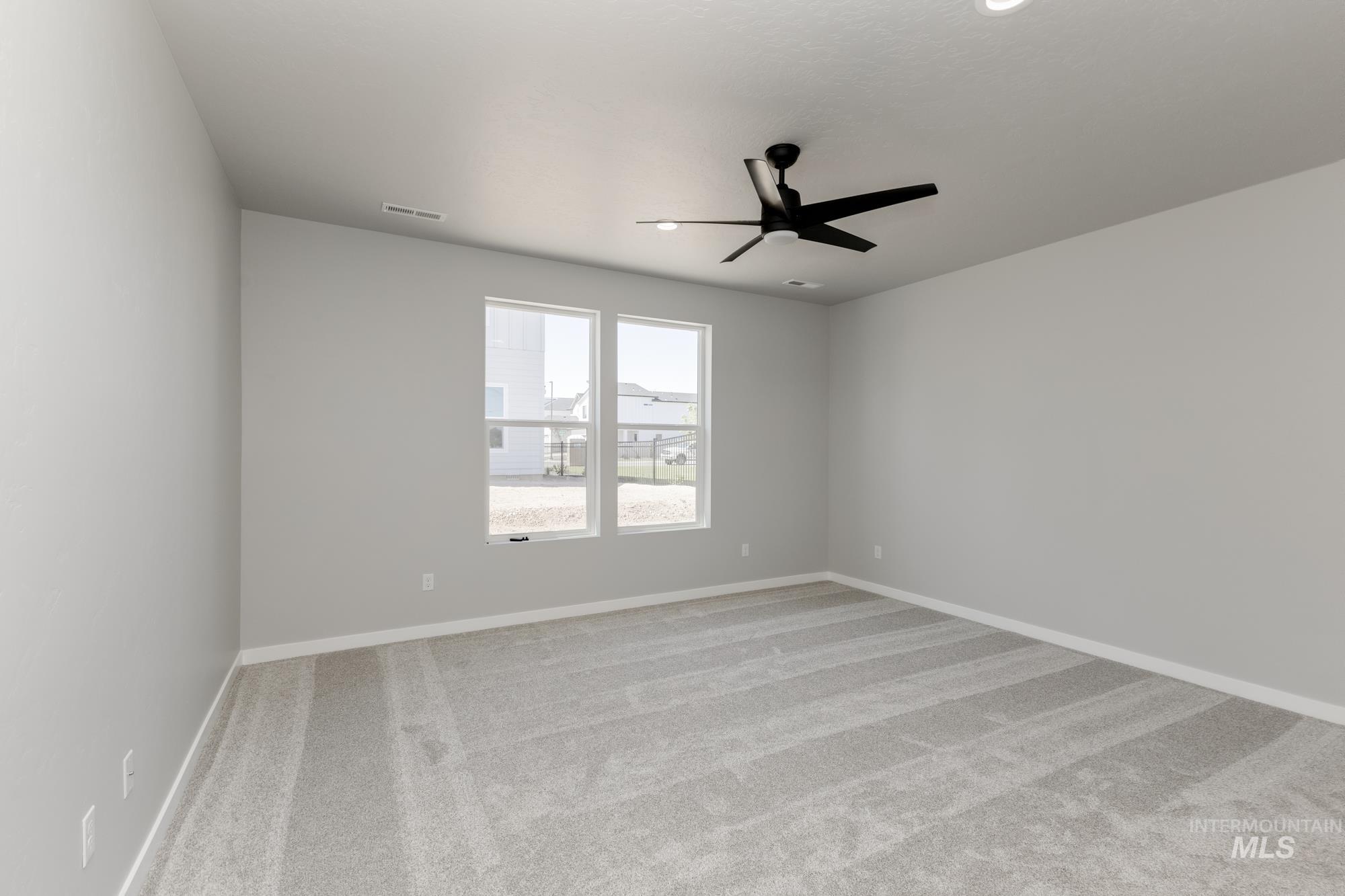 Carpeted spare room featuring ceiling fan and baseboards