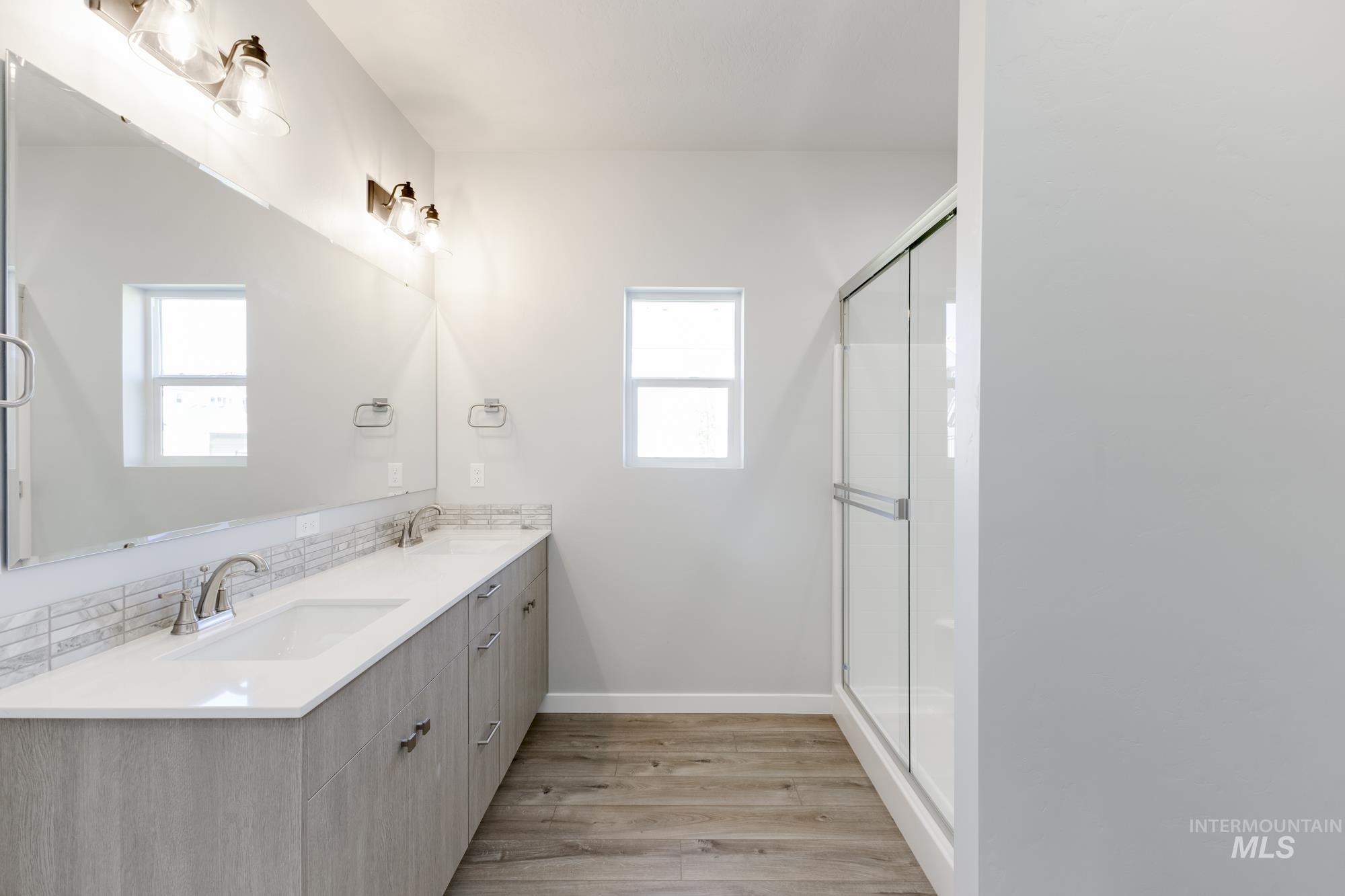 Bathroom featuring double vanity, wood finished floors, and a shower with shower door