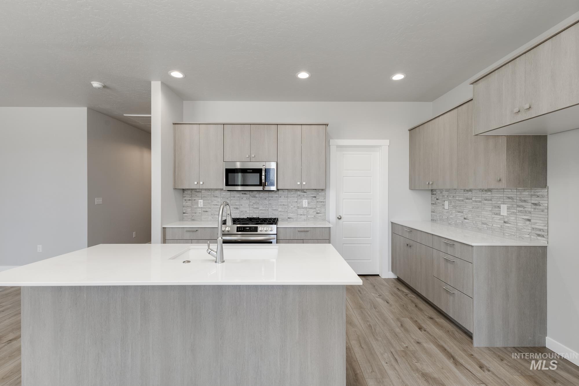 Kitchen featuring modern cabinets, appliances with stainless steel finishes, light wood-style floors, backsplash, and recessed lighting