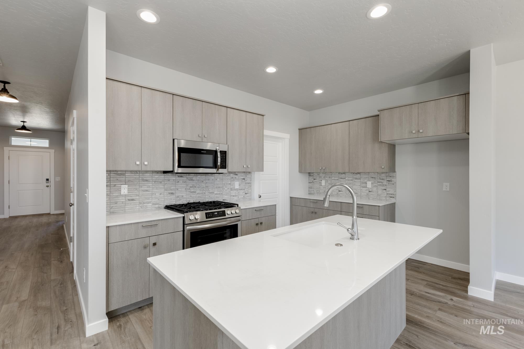 Kitchen with modern cabinets, appliances with stainless steel finishes, light wood-style flooring, decorative backsplash, and light countertops