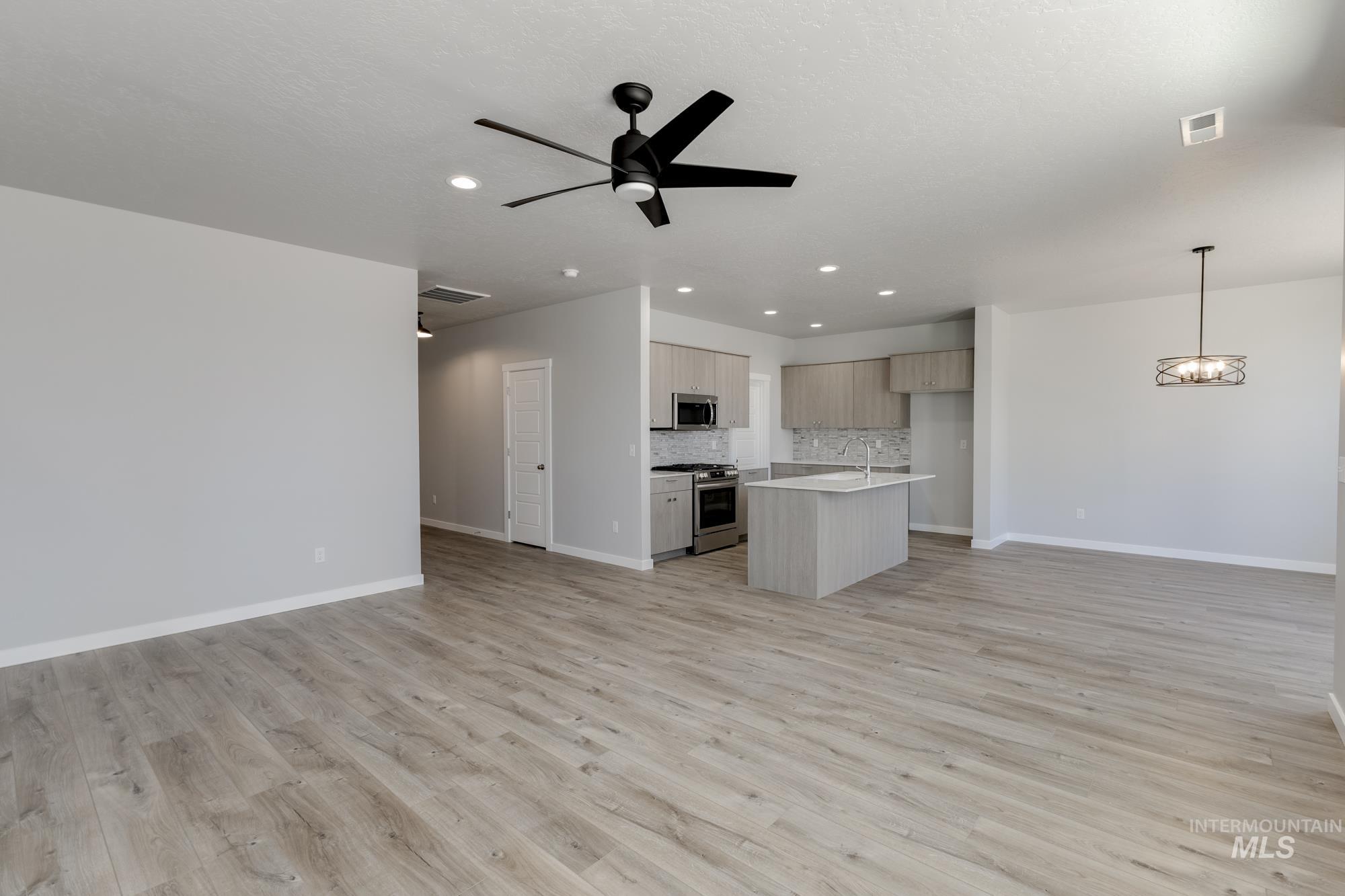 Unfurnished living room featuring recessed lighting, light wood finished floors, a ceiling fan, and a chandelier