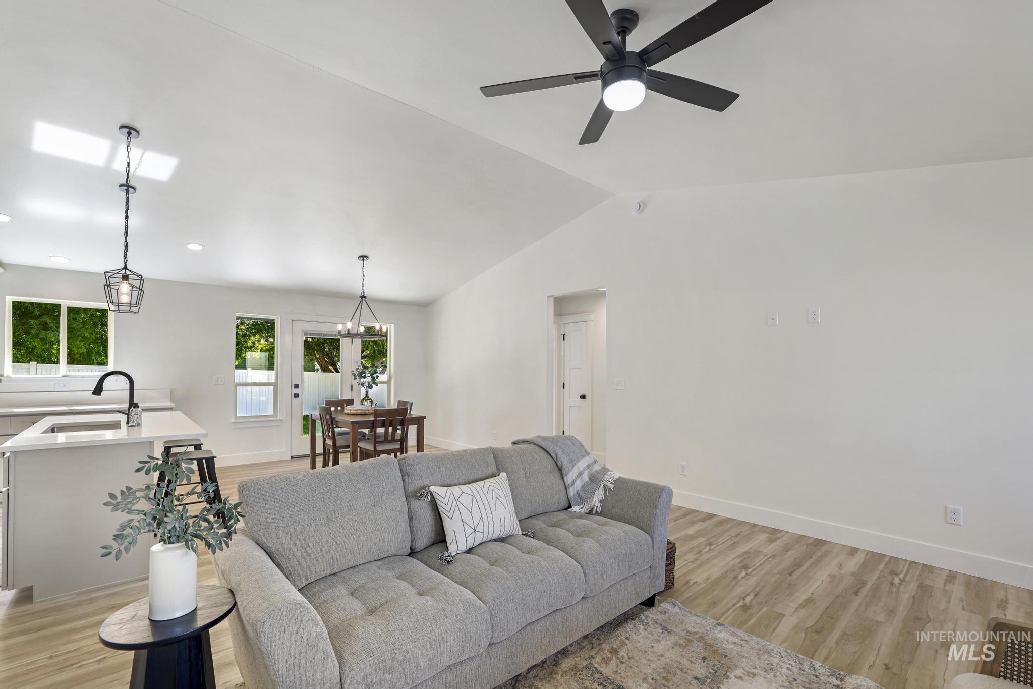 Living room with light wood-type flooring, lofted ceiling, a chandelier, and a ceiling fan