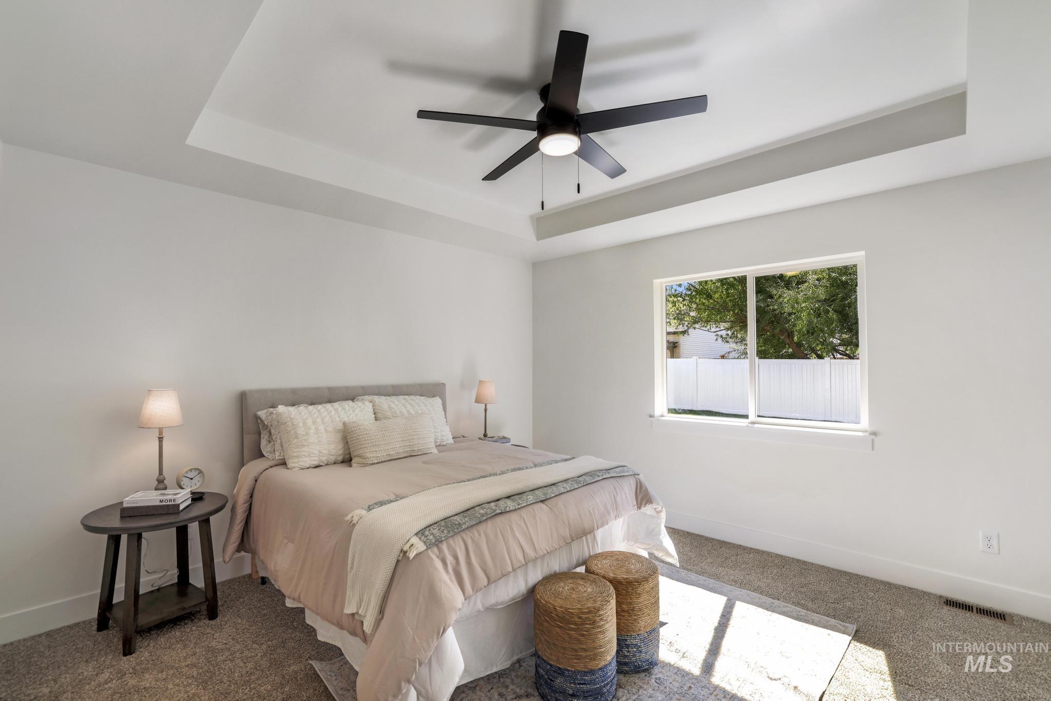 Carpeted bedroom with a tray ceiling and ceiling fan