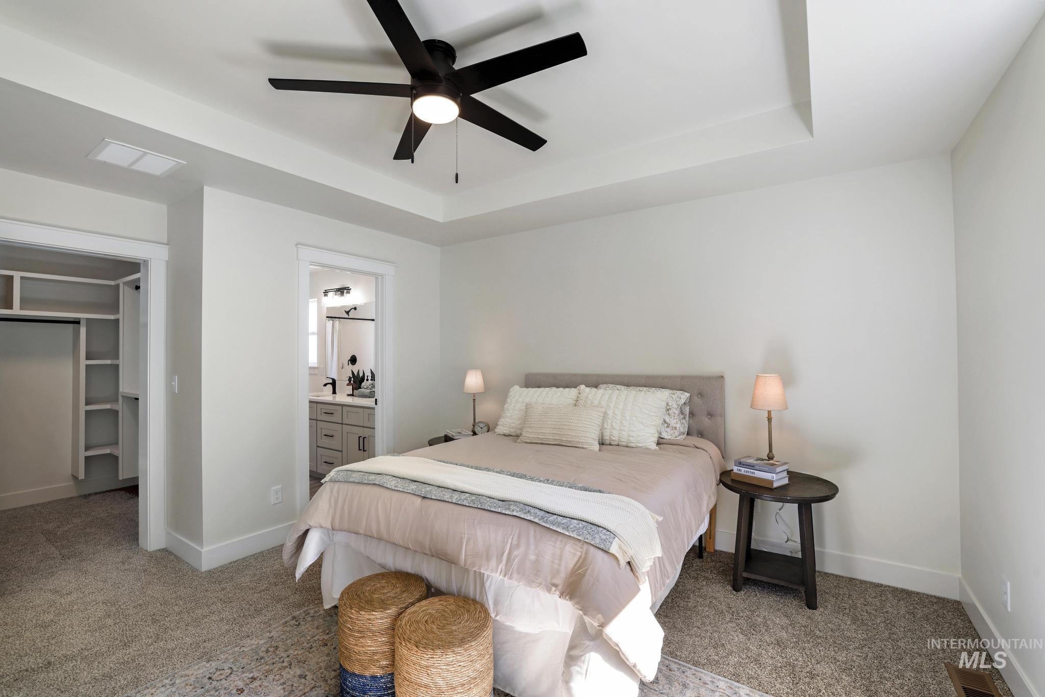 Carpeted bedroom featuring a raised ceiling, a walk in closet, ceiling fan, and connected bathroom