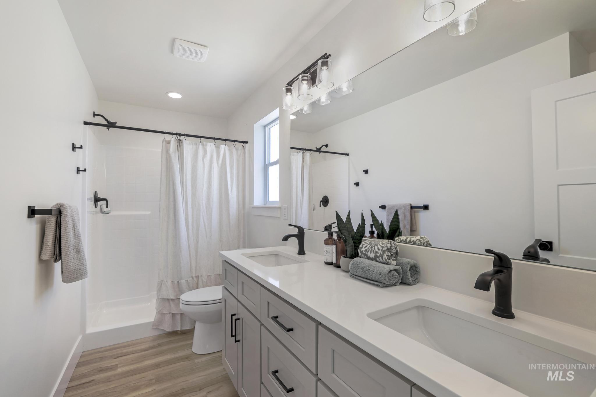 Bathroom with light wood-type flooring, a stall shower, and double vanity