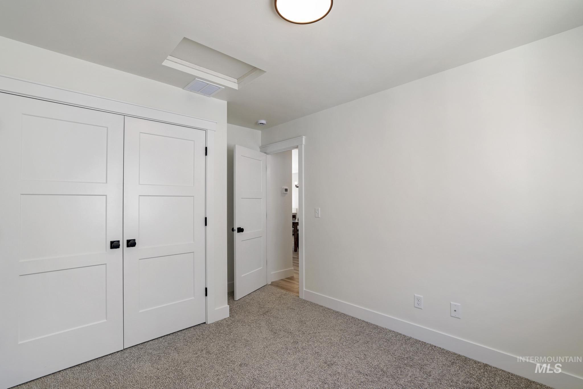 Unfurnished bedroom with carpet, attic access, and a closet