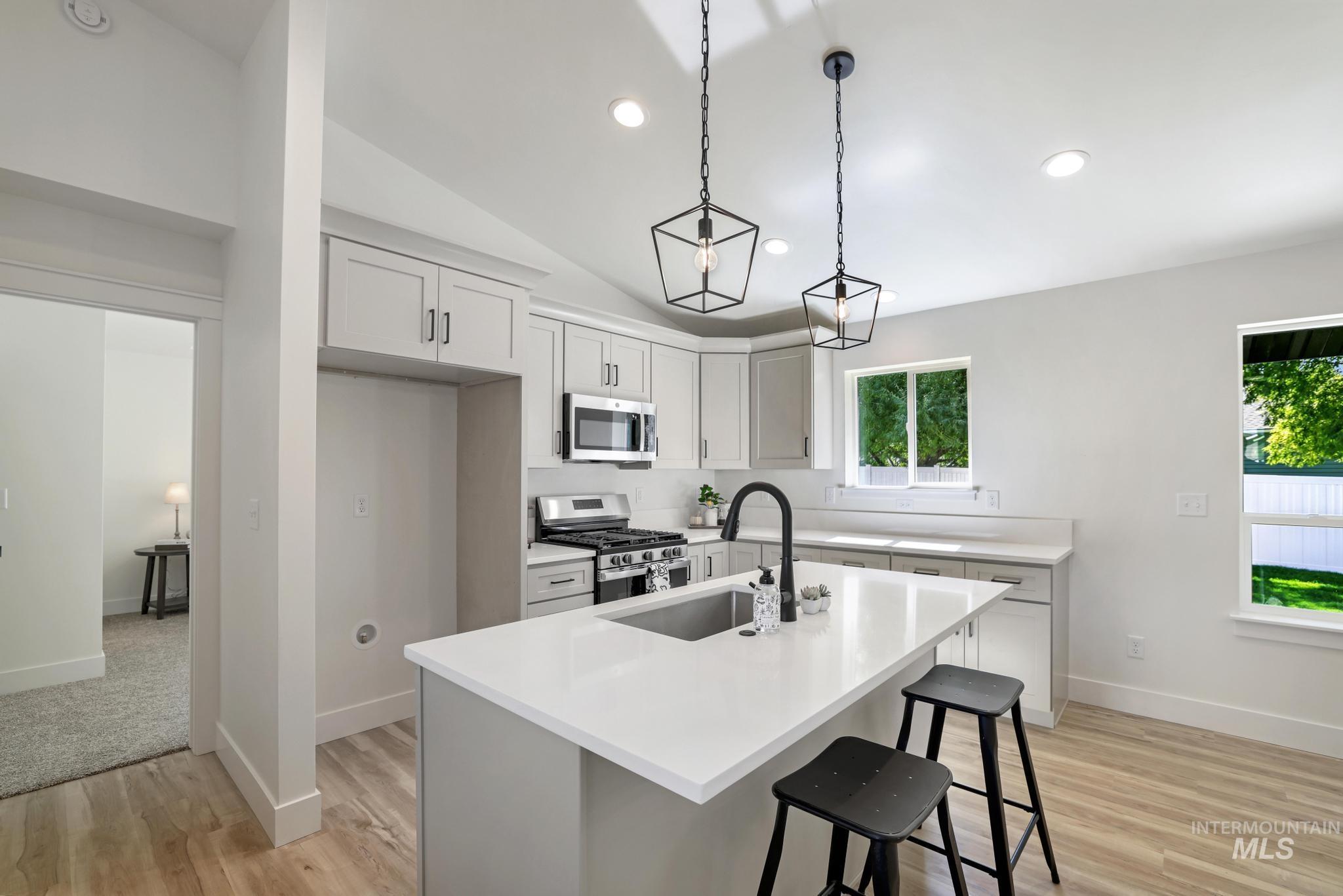 Kitchen with an island with sink, stainless steel appliances, pendant lighting, a breakfast bar, and light wood-type flooring