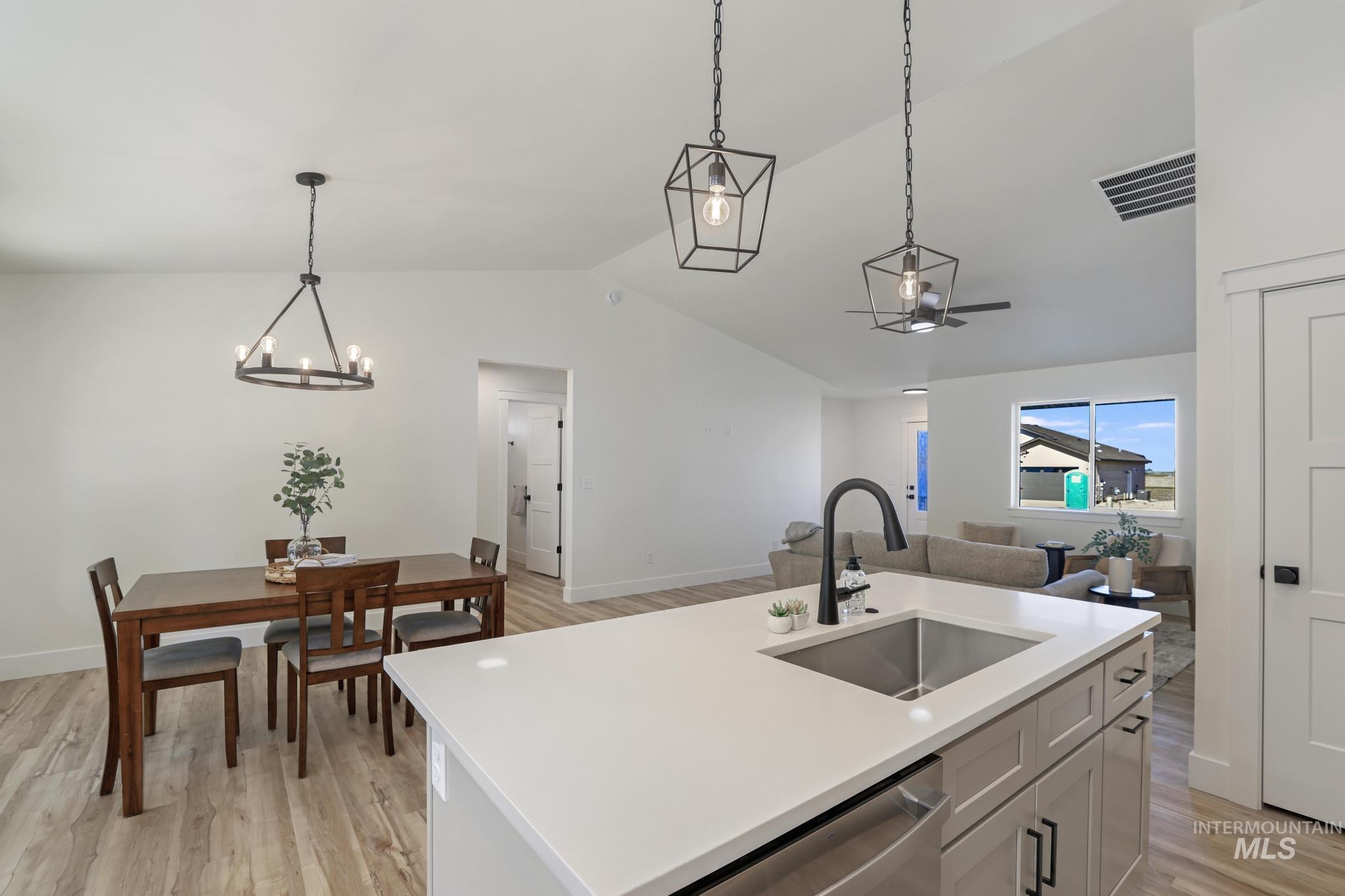 Kitchen with light wood finished floors, vaulted ceiling, pendant lighting, an island with sink, and stainless steel dishwasher