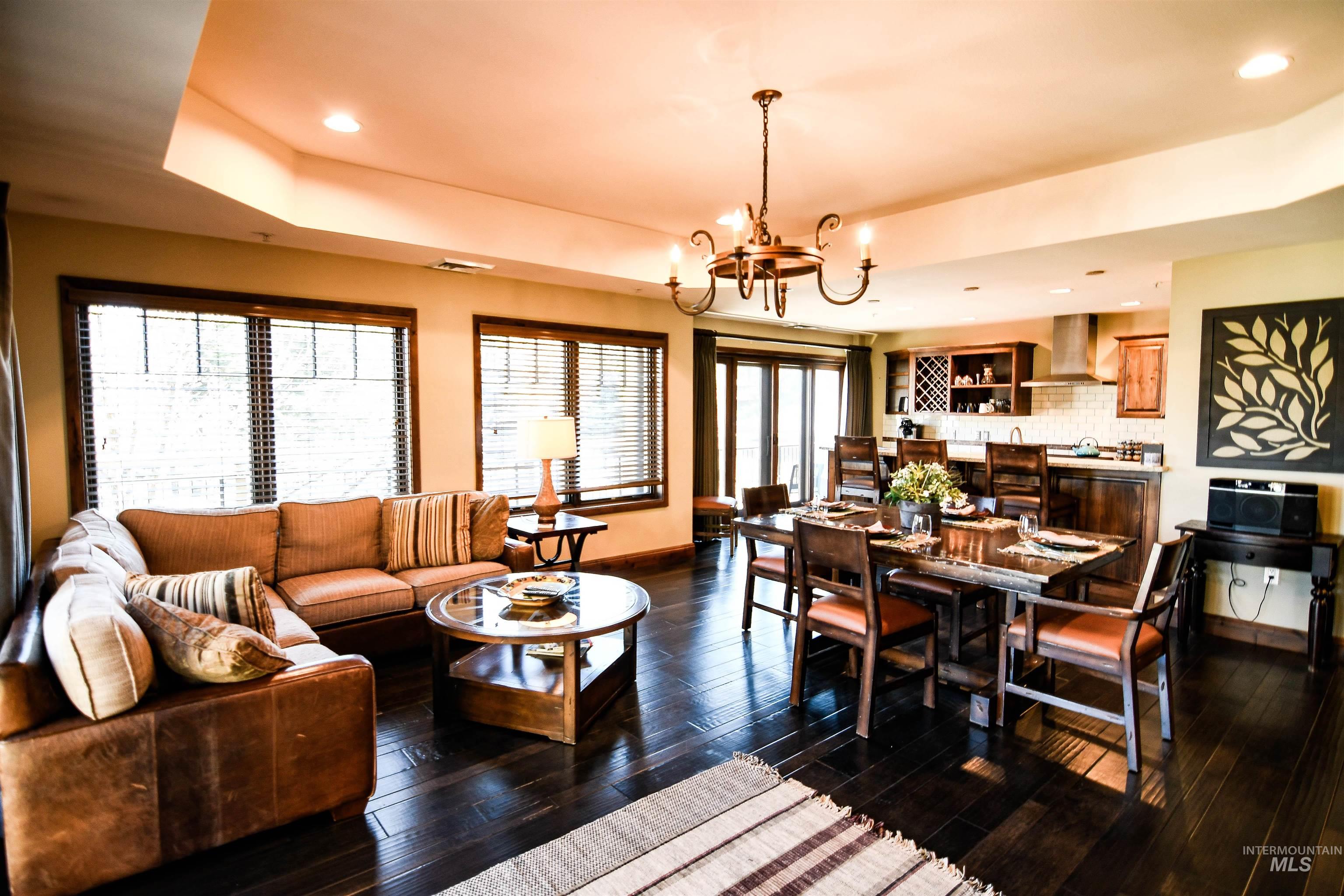 Living area featuring a tray ceiling, dark wood finished floors, recessed lighting, and a chandelier