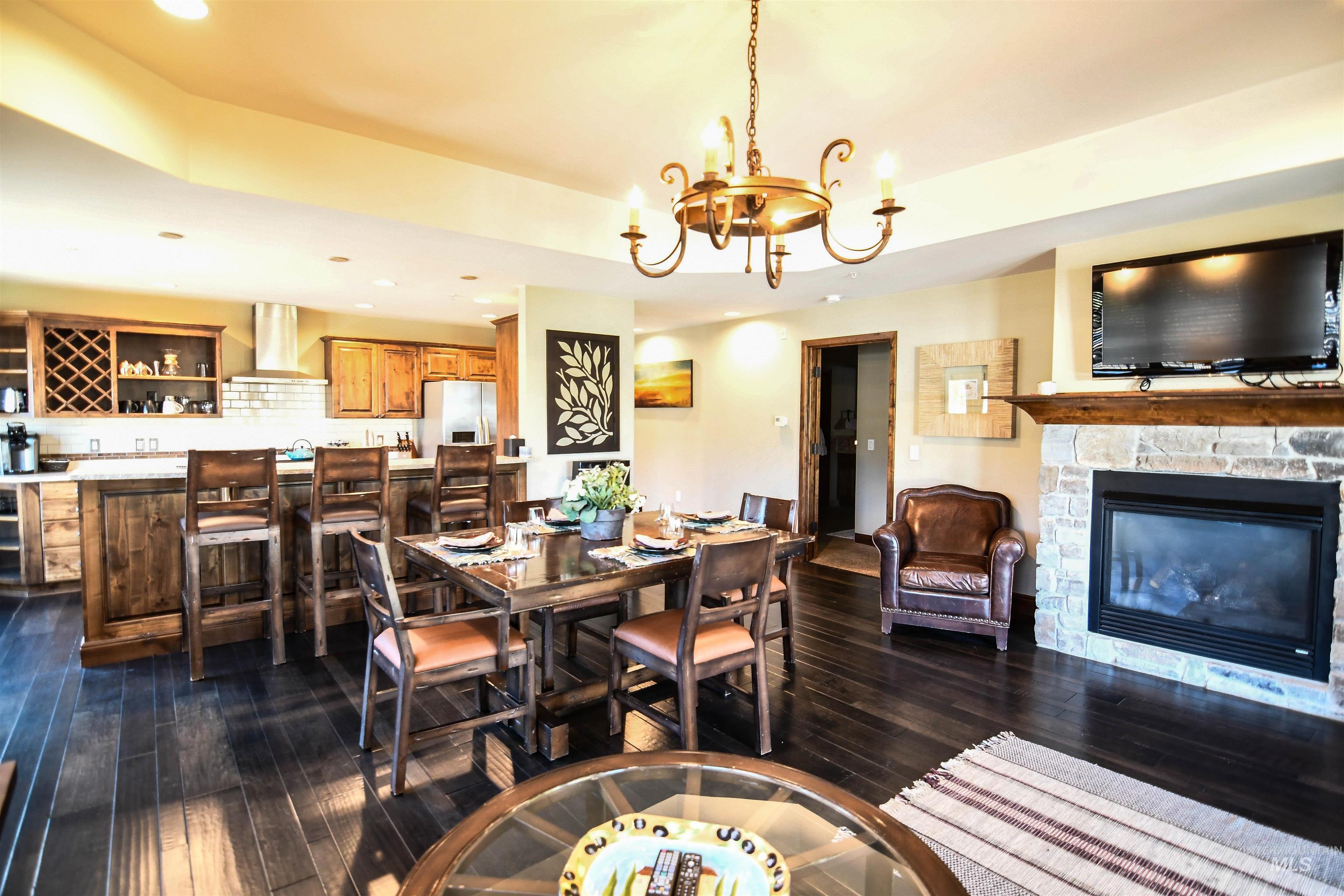 Dining area with dark wood-style floors, recessed lighting, a chandelier, a stone fireplace, and a tray ceiling