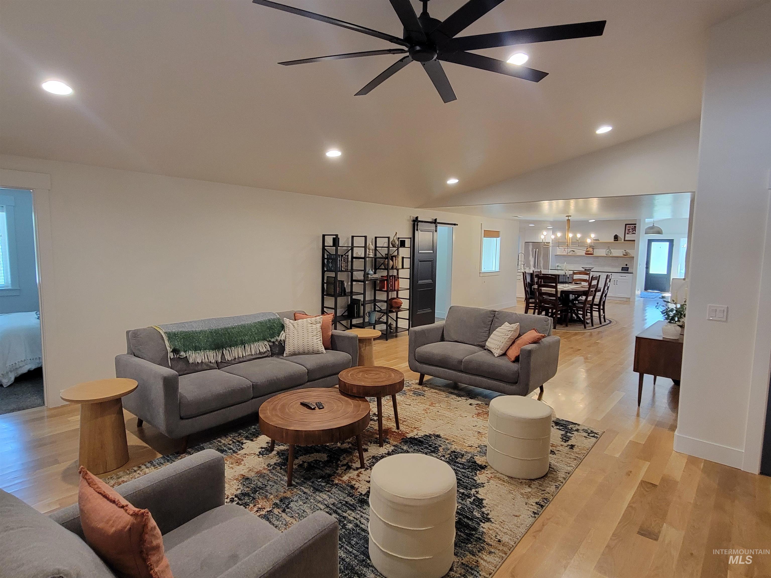 Living area with a barn door, light wood-style floors, recessed lighting, ceiling fan, and a chandelier