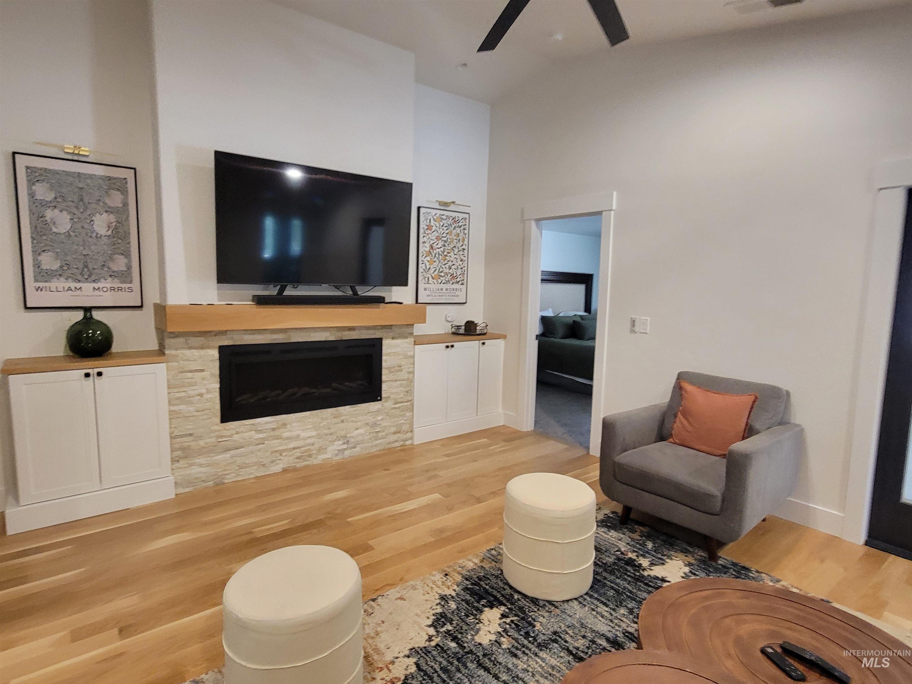 Living room with wood finished floors, ceiling fan, a stone fireplace, and high vaulted ceiling