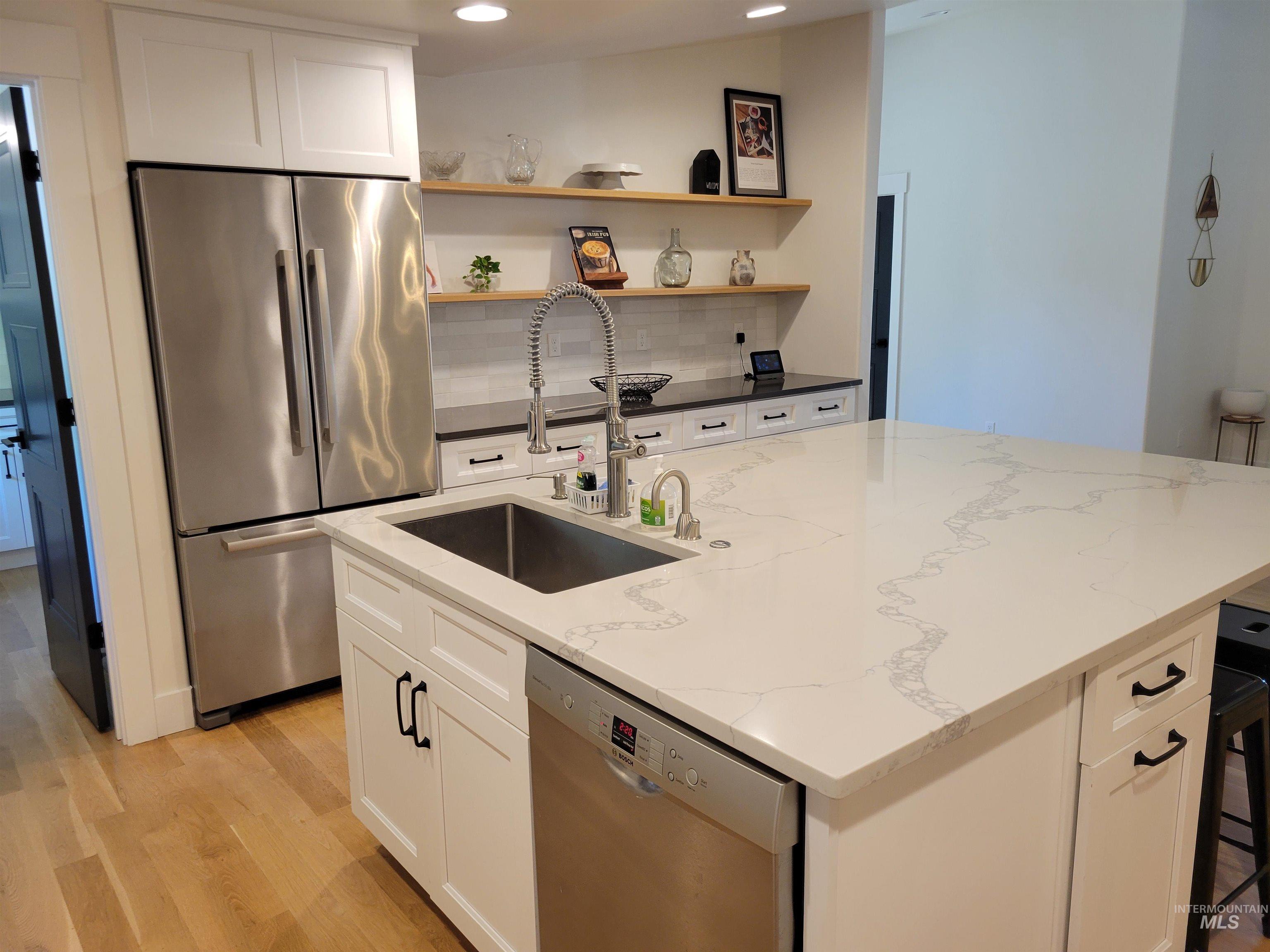 Kitchen with stainless steel appliances, light wood-style flooring, white cabinetry, a kitchen island with sink, and recessed lighting
