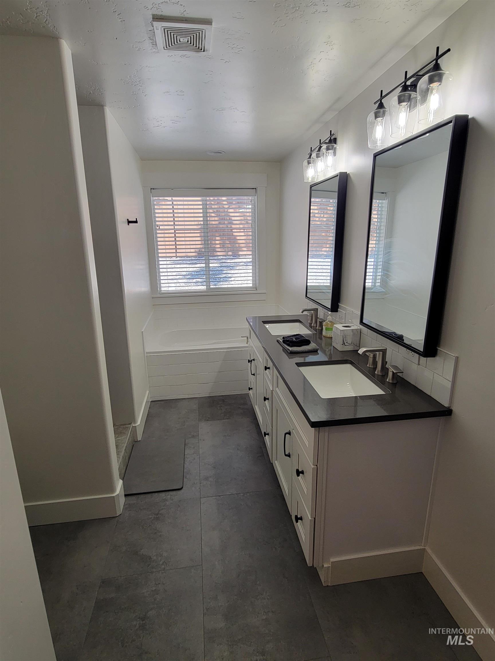 Bathroom with double vanity, a garden tub, and concrete flooring