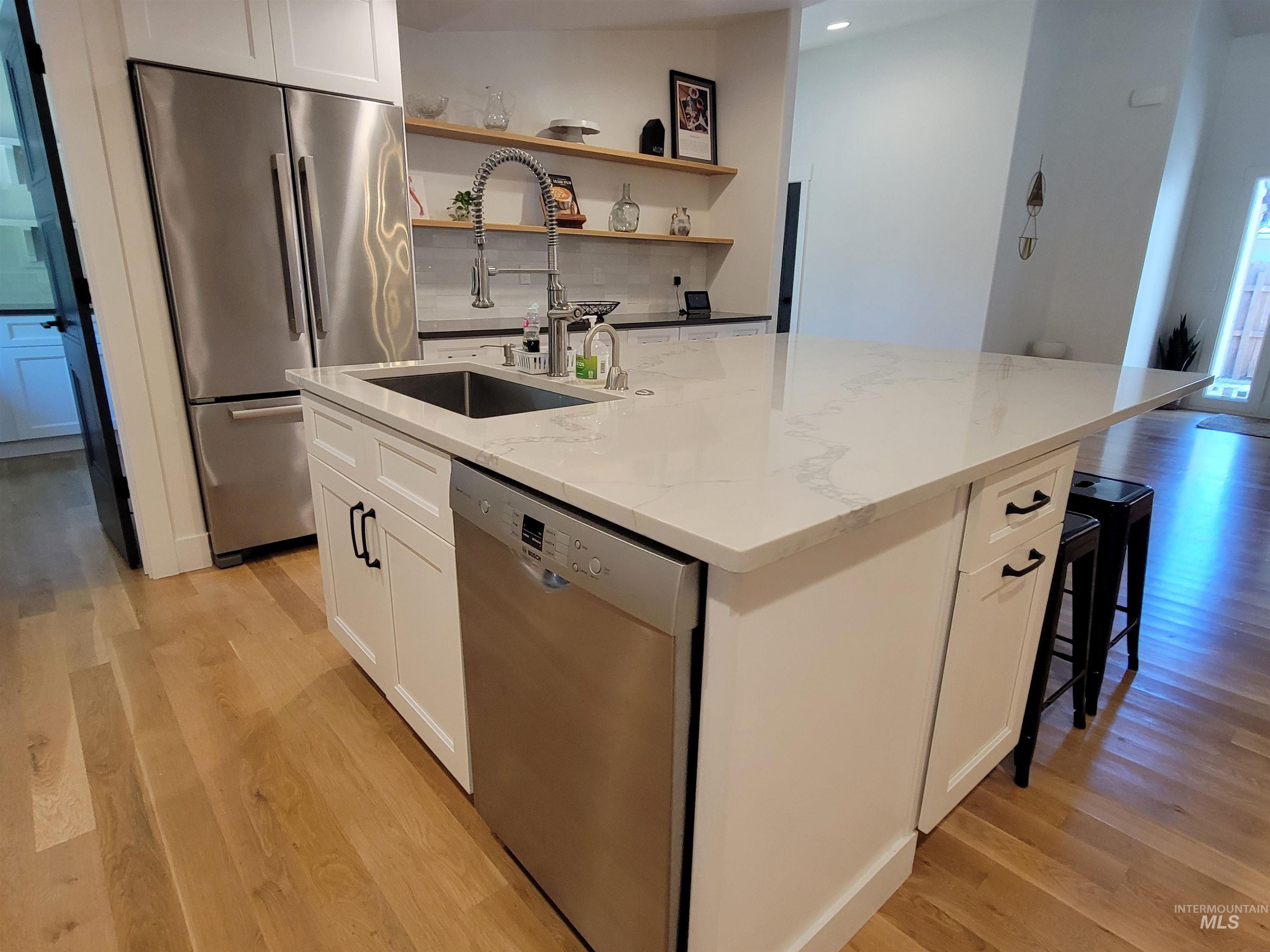 Kitchen with appliances with stainless steel finishes, light wood-style floors, a kitchen island with sink, white cabinets, and recessed lighting