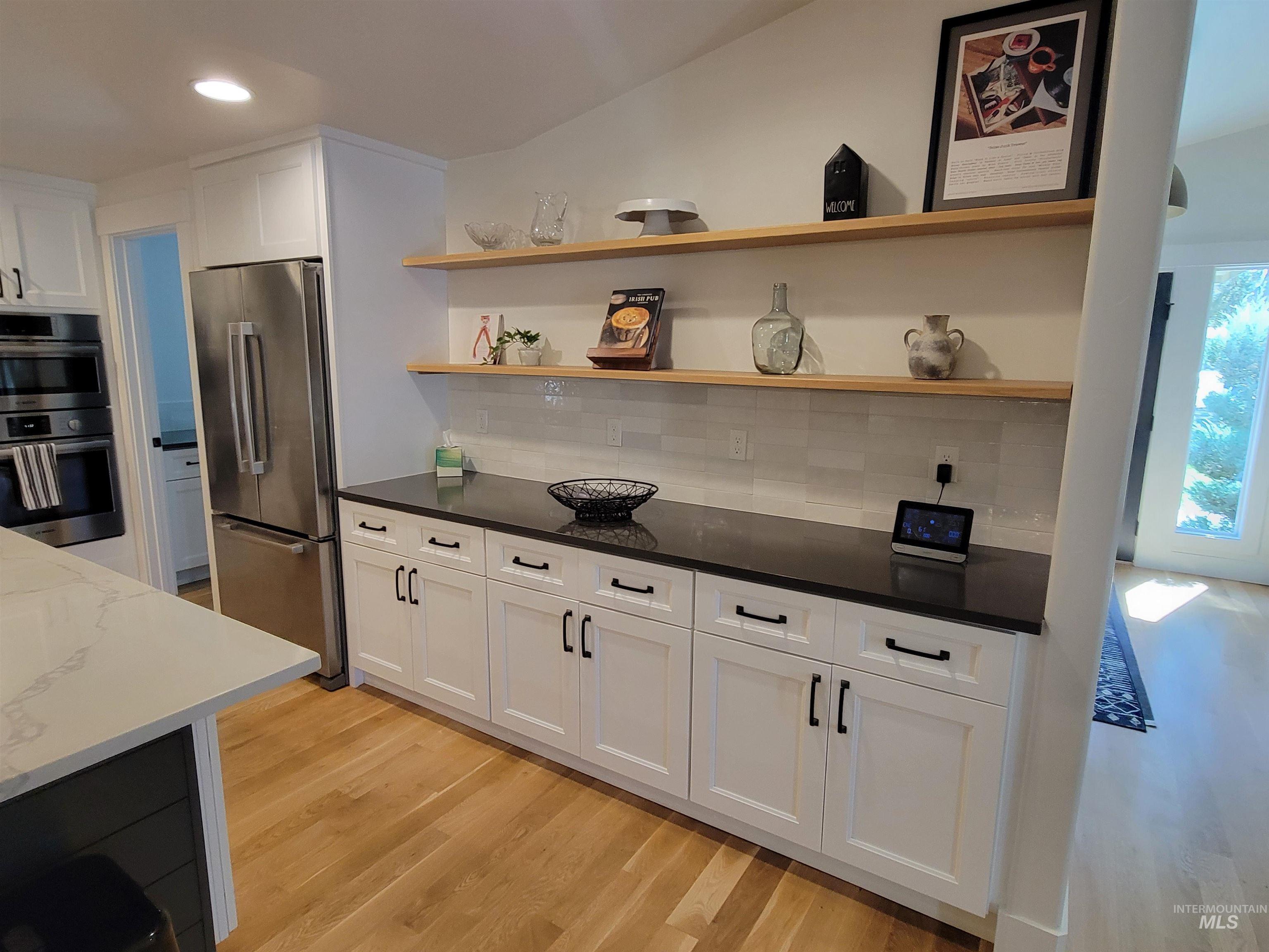 Kitchen with open shelves, light wood-style flooring, stainless steel appliances, tasteful backsplash, and white cabinets