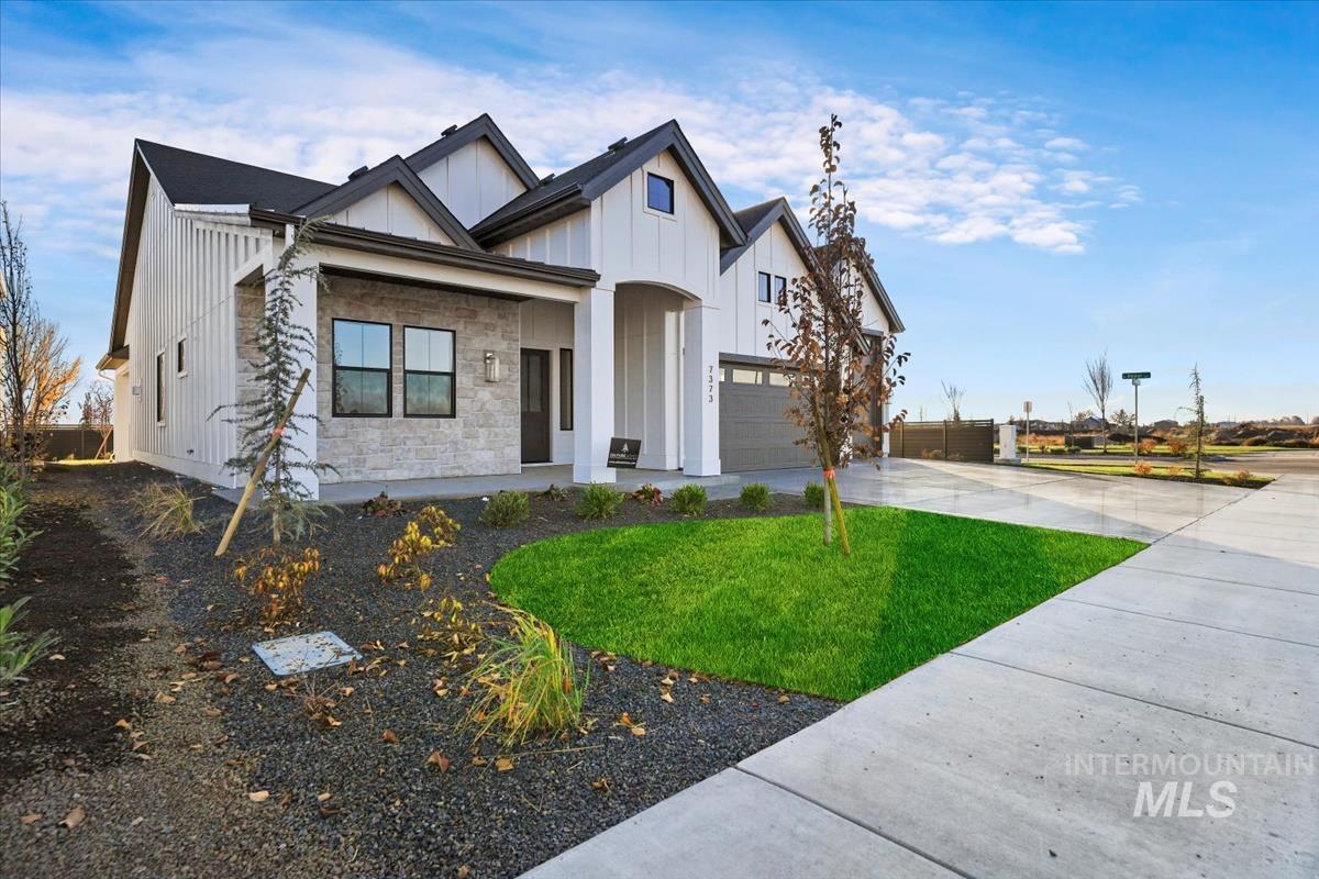 Modern farmhouse with board and batten siding, stone siding, driveway, and a front lawn