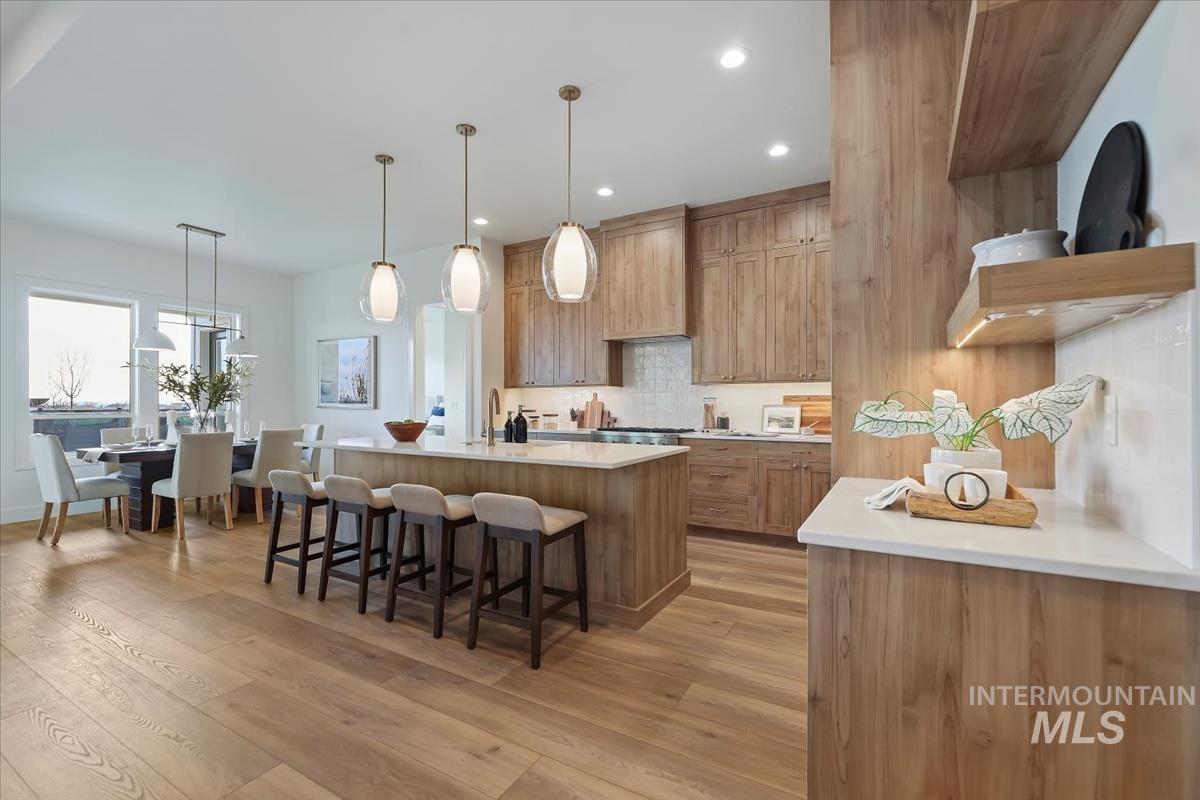 Kitchen with tasteful backsplash, a kitchen island with sink, decorative light fixtures, a breakfast bar area, and light wood-style floors