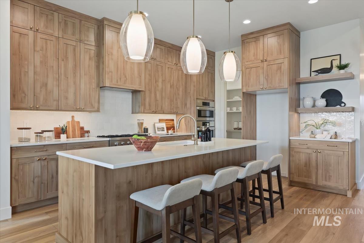 Kitchen featuring tasteful backsplash, open shelves, light wood finished floors, a center island with sink, and recessed lighting