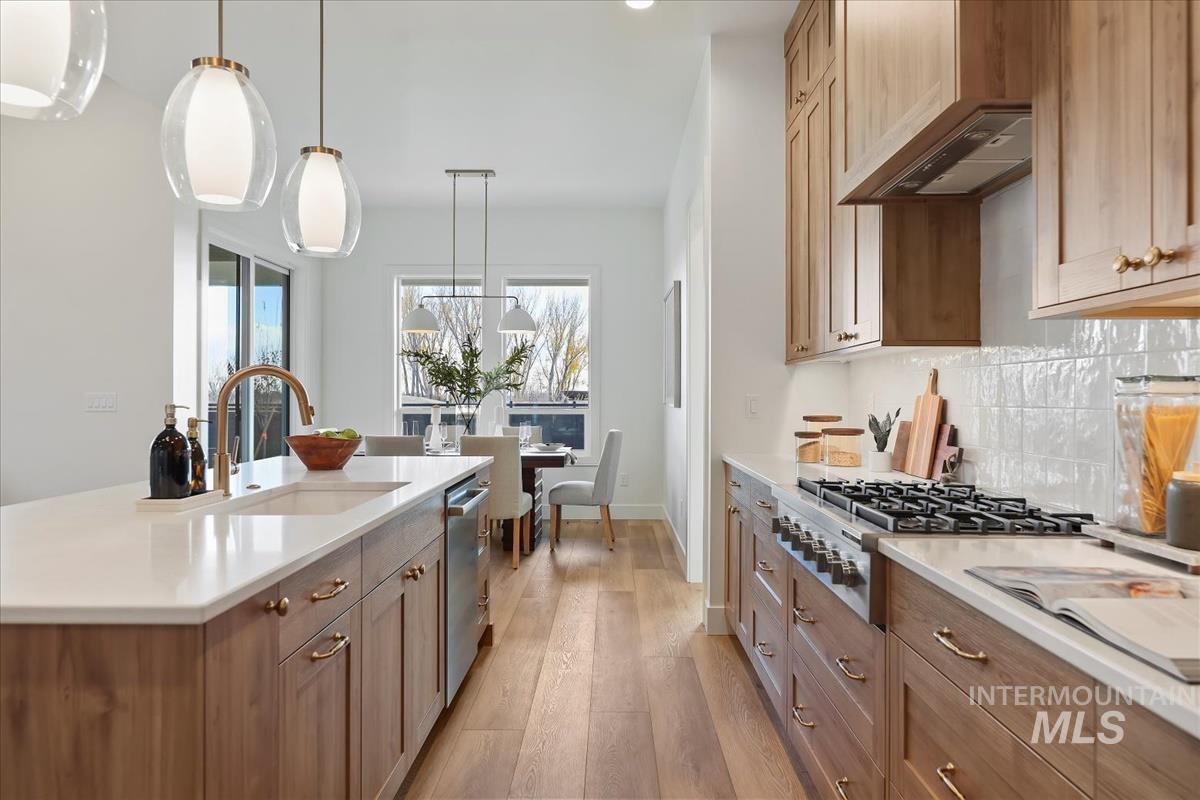Kitchen with pendant lighting, light wood finished floors, brown cabinets, appliances with stainless steel finishes, and backsplash