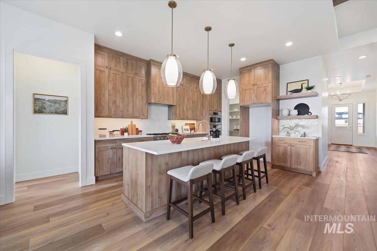 Kitchen featuring a breakfast bar, light wood-type flooring, hanging light fixtures, a center island with sink, and recessed lighting