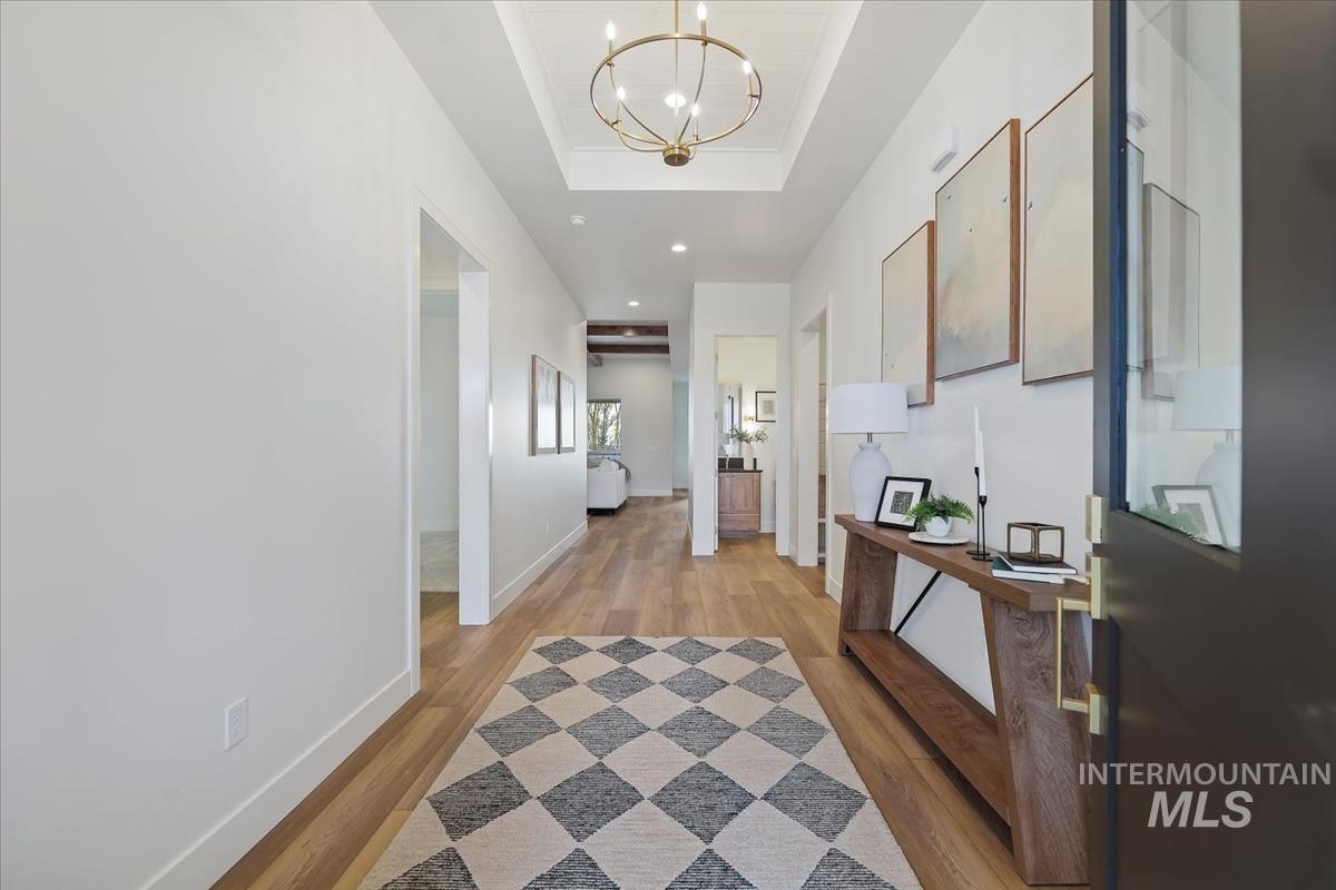 Hallway featuring light wood finished floors, a tray ceiling, and a chandelier