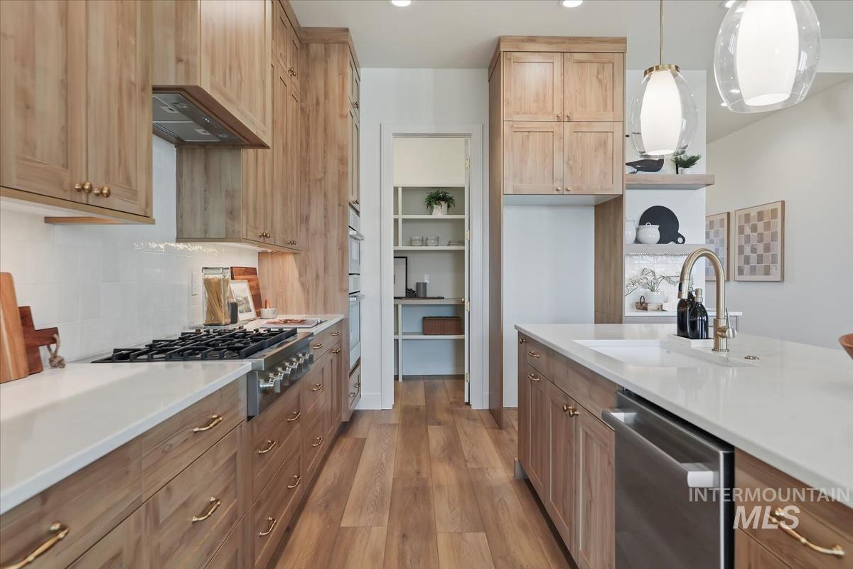 Kitchen with light wood finished floors, stainless steel appliances, hanging light fixtures, open shelves, and light stone counters