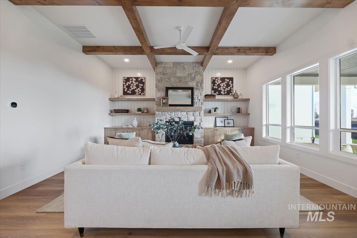 Living room featuring wood finished floors, beamed ceiling, a ceiling fan, coffered ceiling, and a fireplace