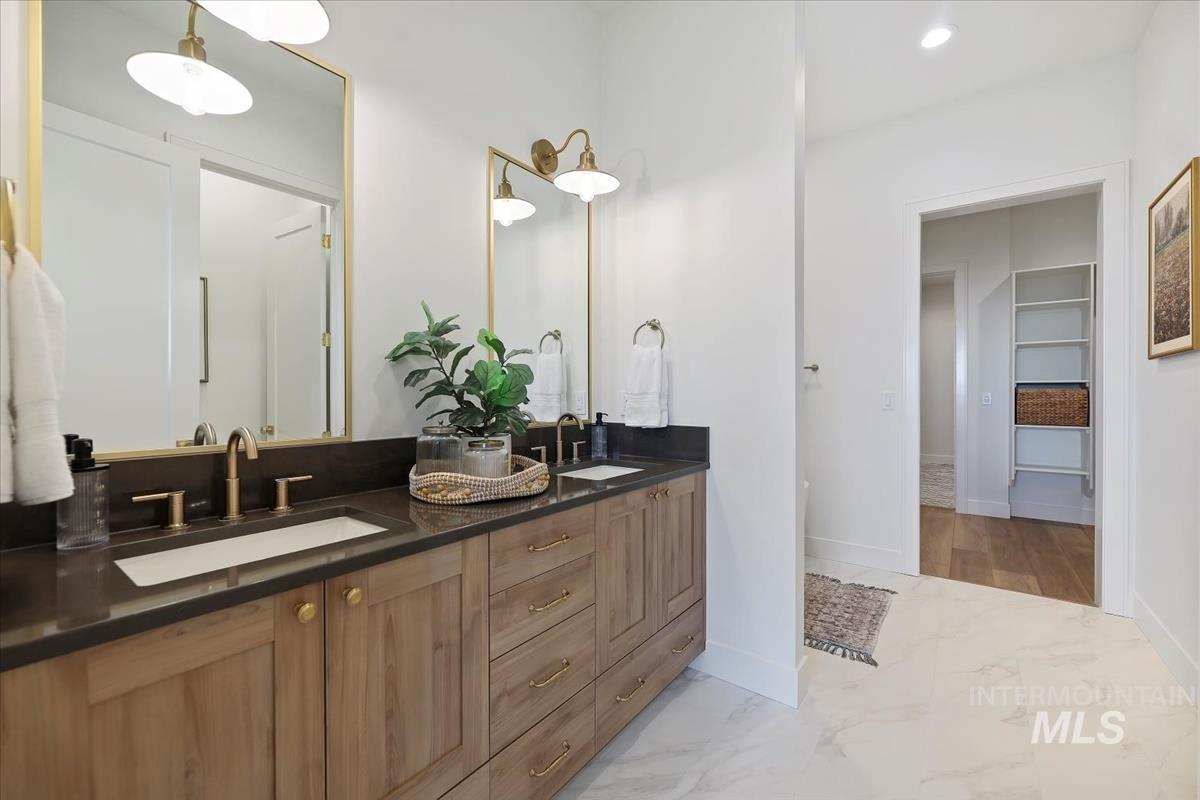 Bathroom with double vanity, light marble finish flooring, a walk in closet, and recessed lighting