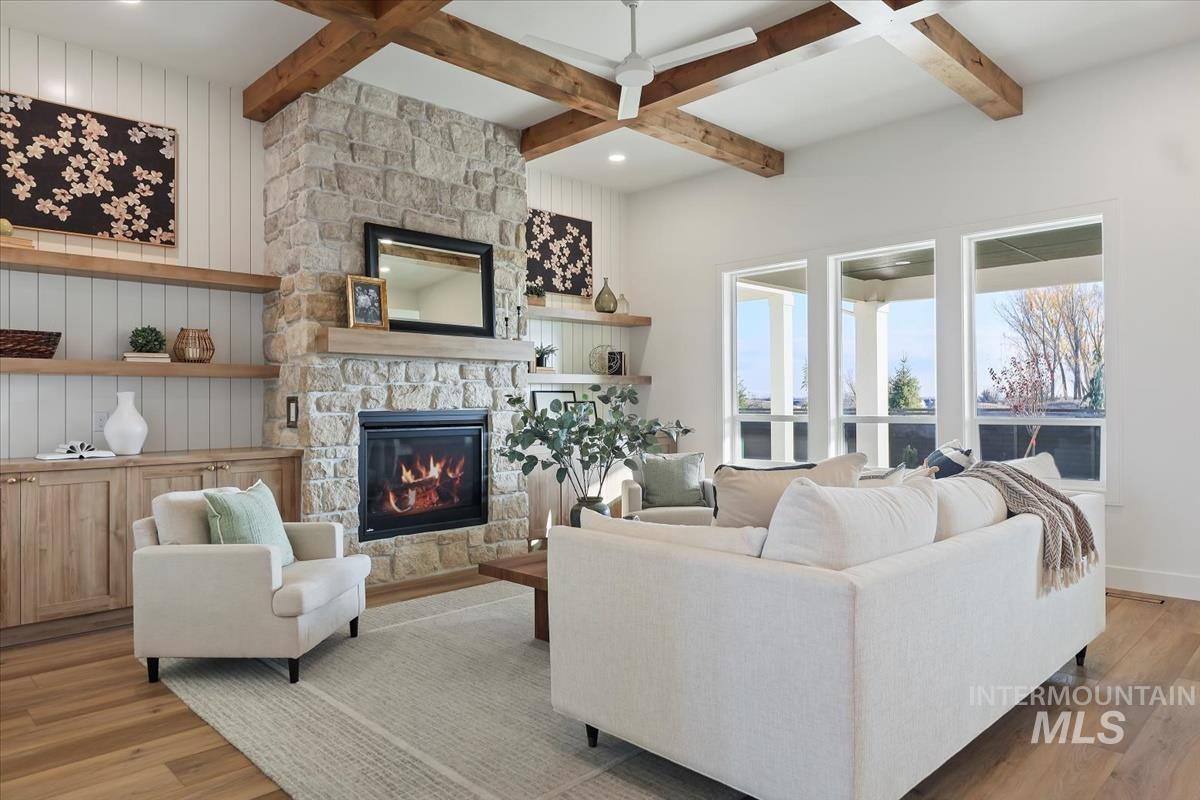 Living area with light wood finished floors, beamed ceiling, a stone fireplace, and coffered ceiling