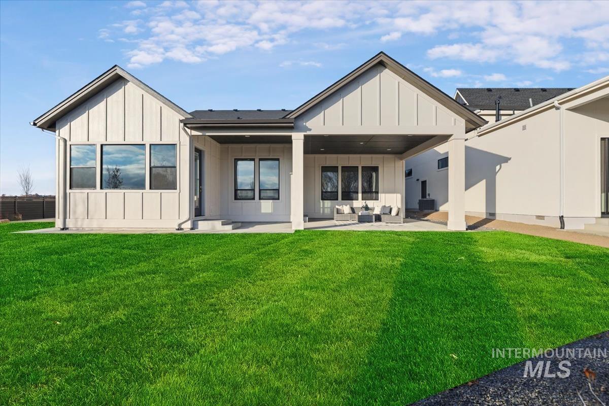 Rear view of house with board and batten siding, a patio area, a lawn, and an outdoor hangout area