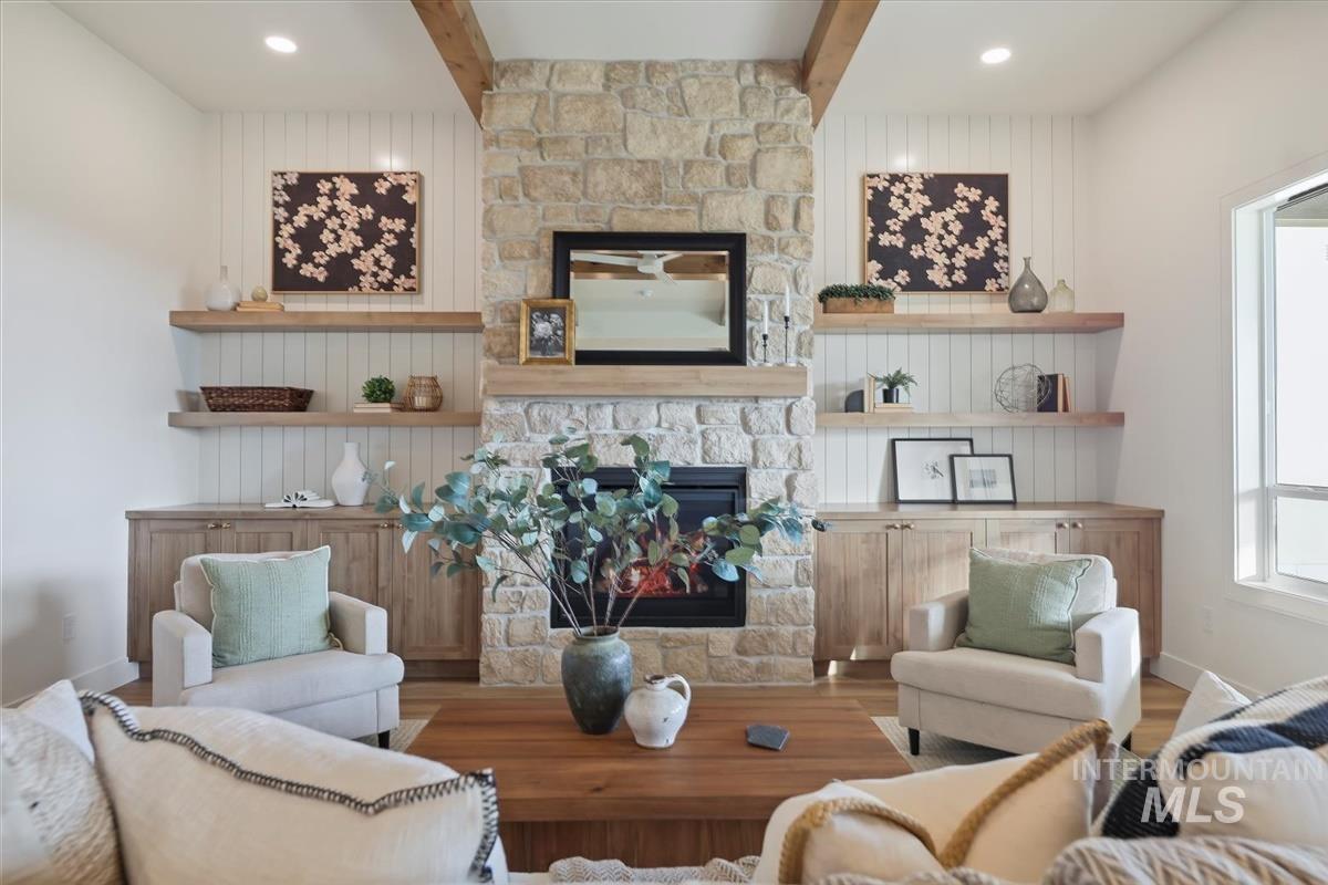 Living room with beam ceiling, a stone fireplace, wood finished floors, healthy amount of natural light, and wooden walls