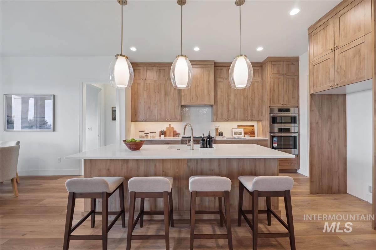 Kitchen with a kitchen breakfast bar, hanging light fixtures, a center island with sink, light wood-type flooring, and light brown cabinetry